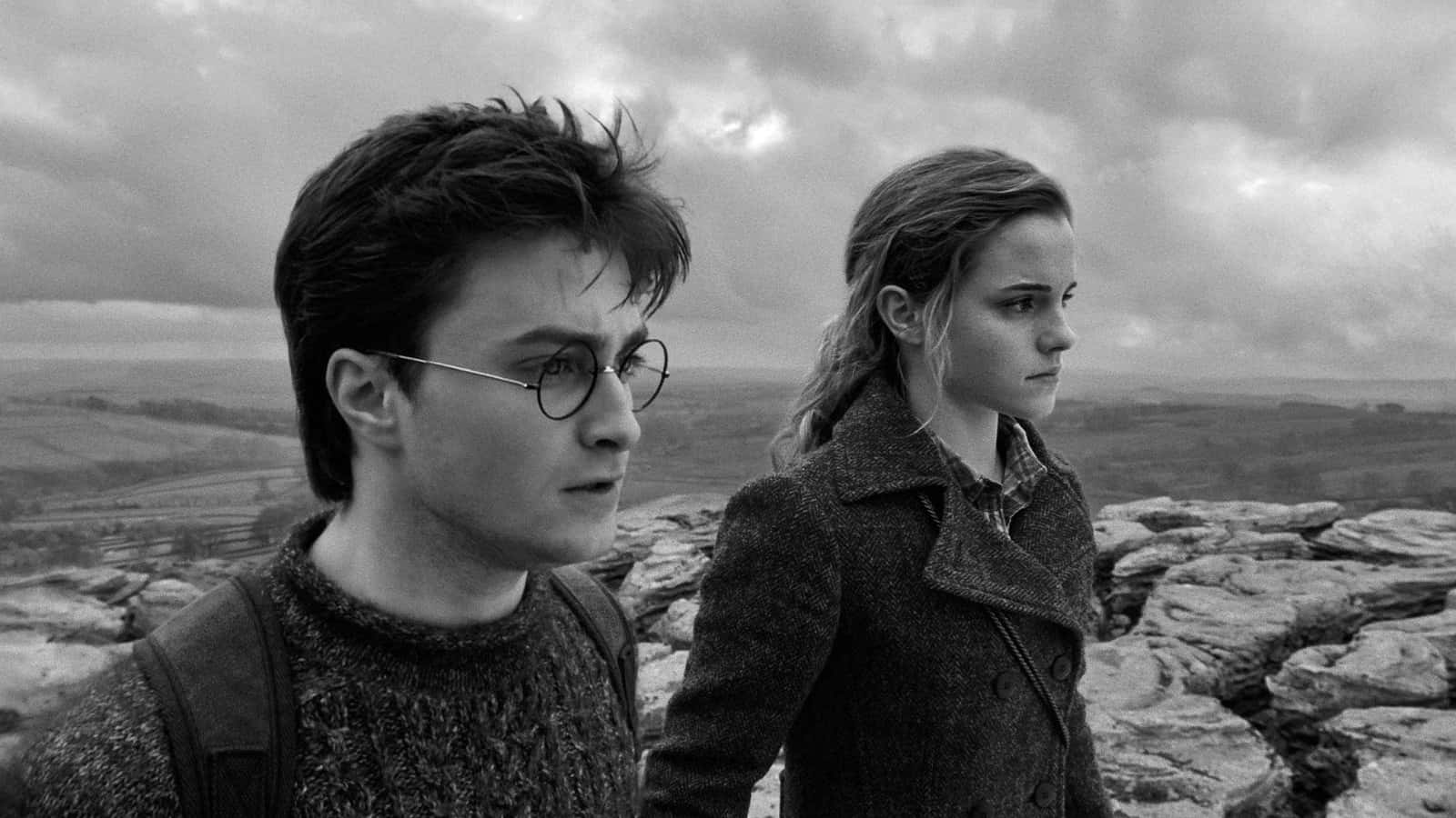The Wizarding War 桌布 壁紙 — 兩位年輕成年人並肩站在岩石山頂上，在陰天凝視遠方。