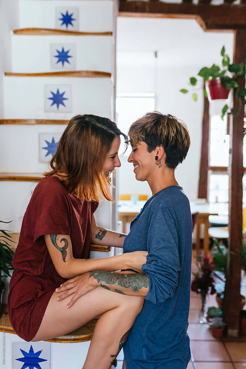Happy Couples 桌布 壁紙 — 兩位微笑的刺青女性在裝飾著藍色星星的木樓梯上溫暖地擁抱。
