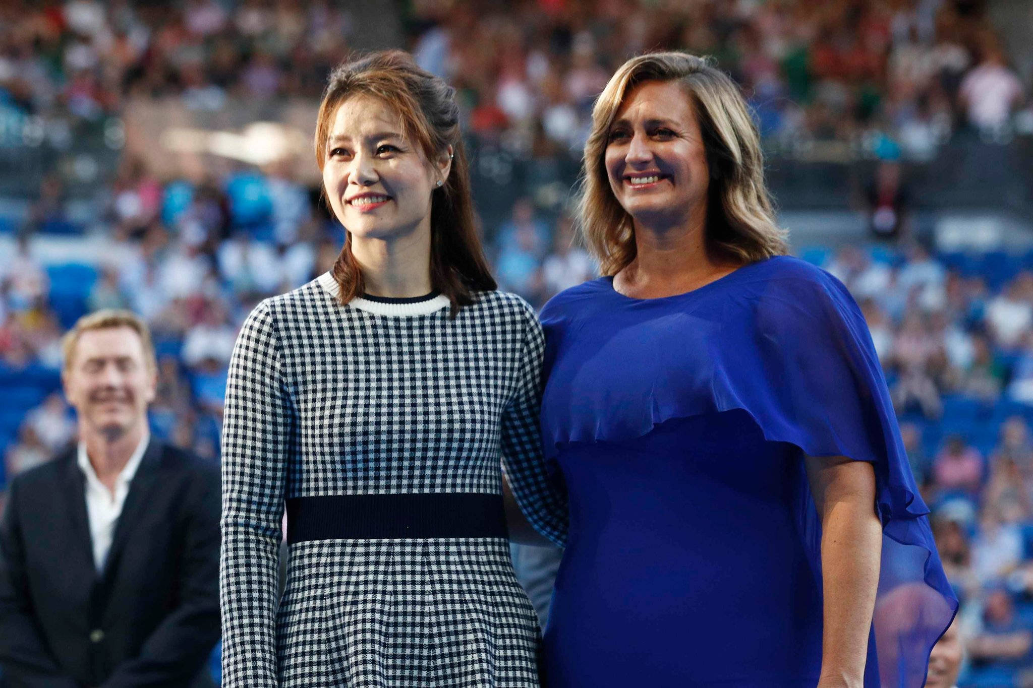 Australian Open 桌布 壁紙 — 兩位微笑的女性並肩站在體育館內，身後是模糊的人群。