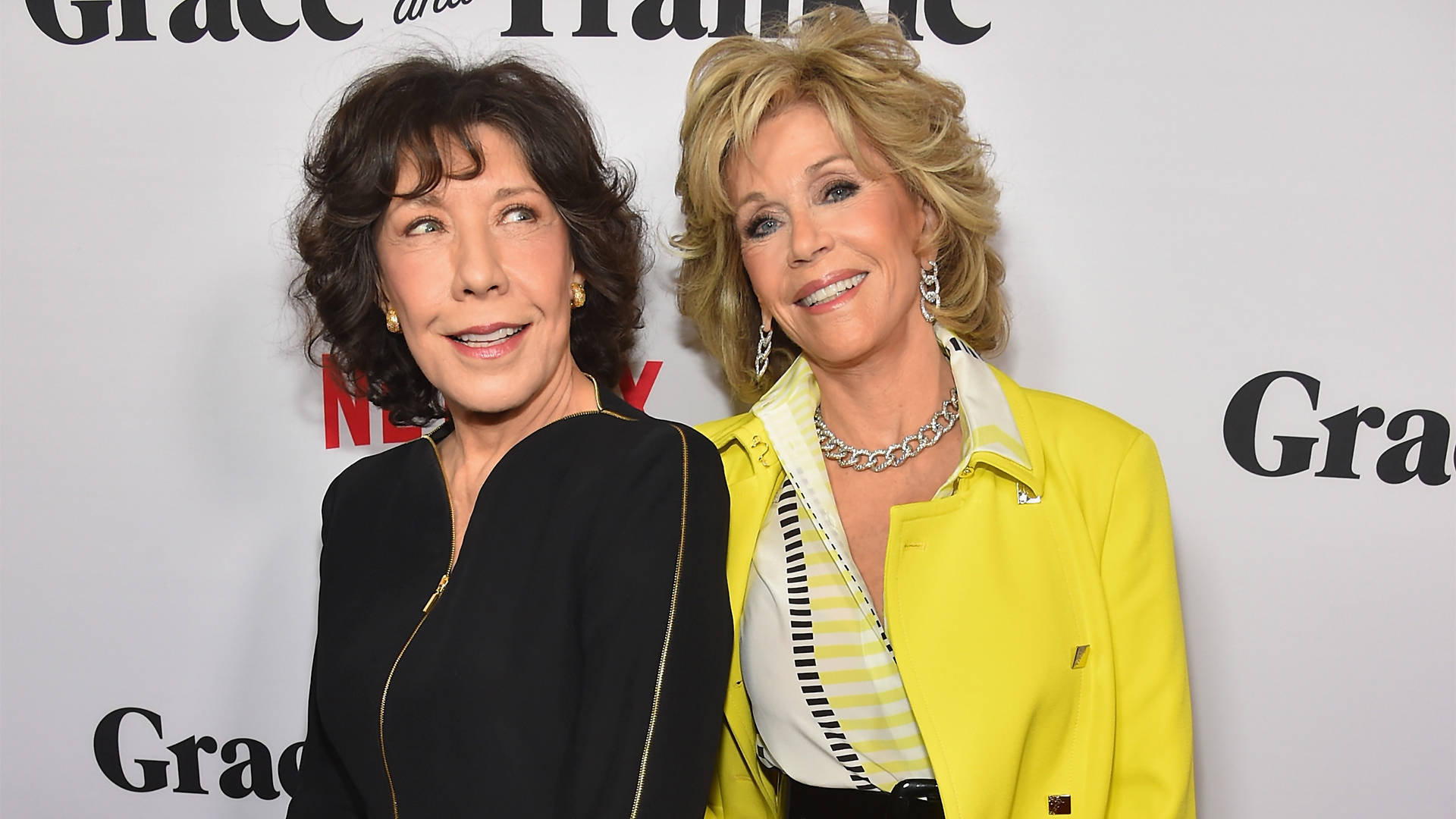 女演員 桌布 壁紙 — 兩位微笑的女性在「Grace and Frankie」活動中擺姿勢，一位穿黑色，另一位穿亮黃色外套。