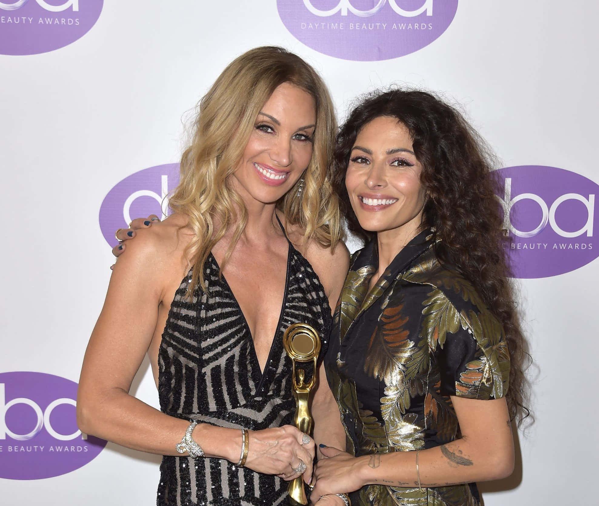 sarah shahi 桌布 壁紙 — 兩位微笑的女性在日間美容獎頒獎典禮上一起擺姿勢，其中一人手持金色獎盃，背景為品牌標誌。