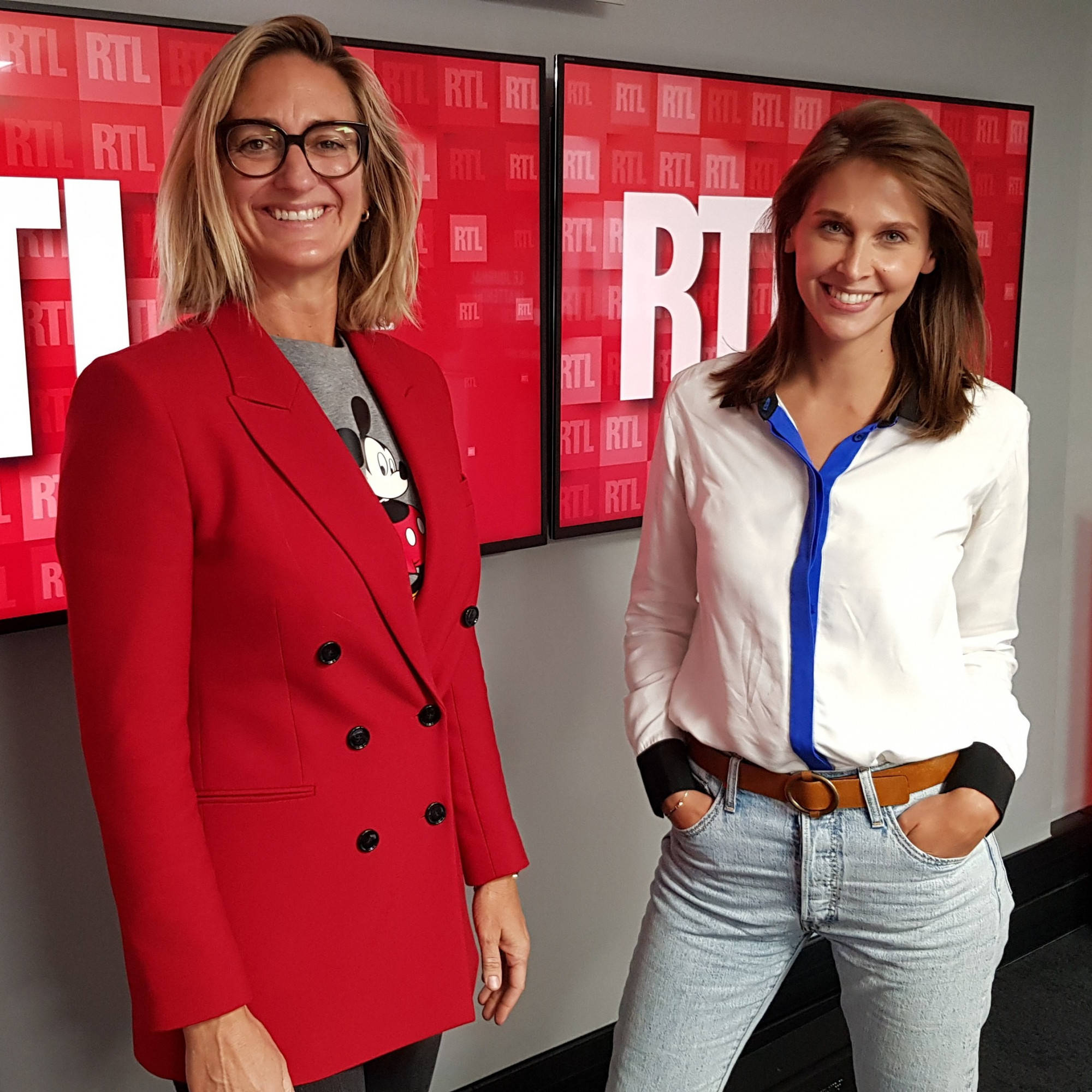 Tennis 桌布 壁紙 — 兩位微笑的女性在紅色RTL品牌螢幕前擺姿勢，一位穿著紅色西裝外套內搭米奇老鼠T恤，另一位穿著白色襯衫和牛仔褲。