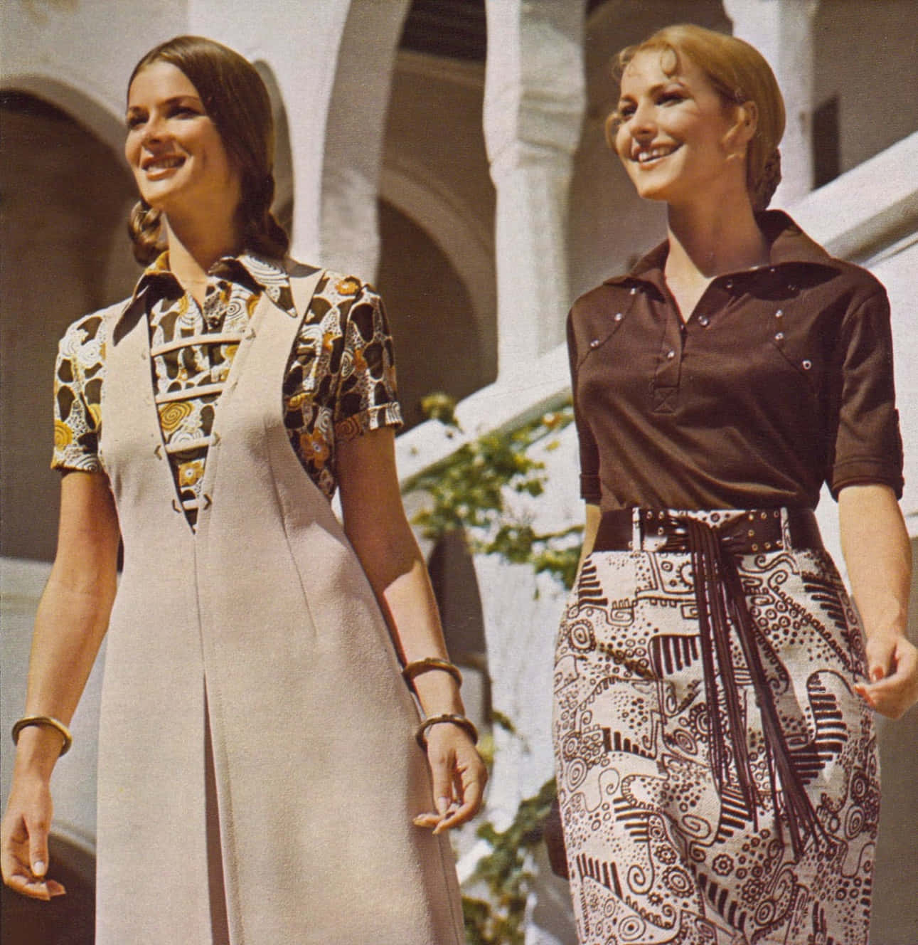 70年代動圖 桌布 壁紙 — 兩位微笑的女性穿著1970年代圖案服裝，在陽光普照的樹葉下漫步於白色拱門之間。