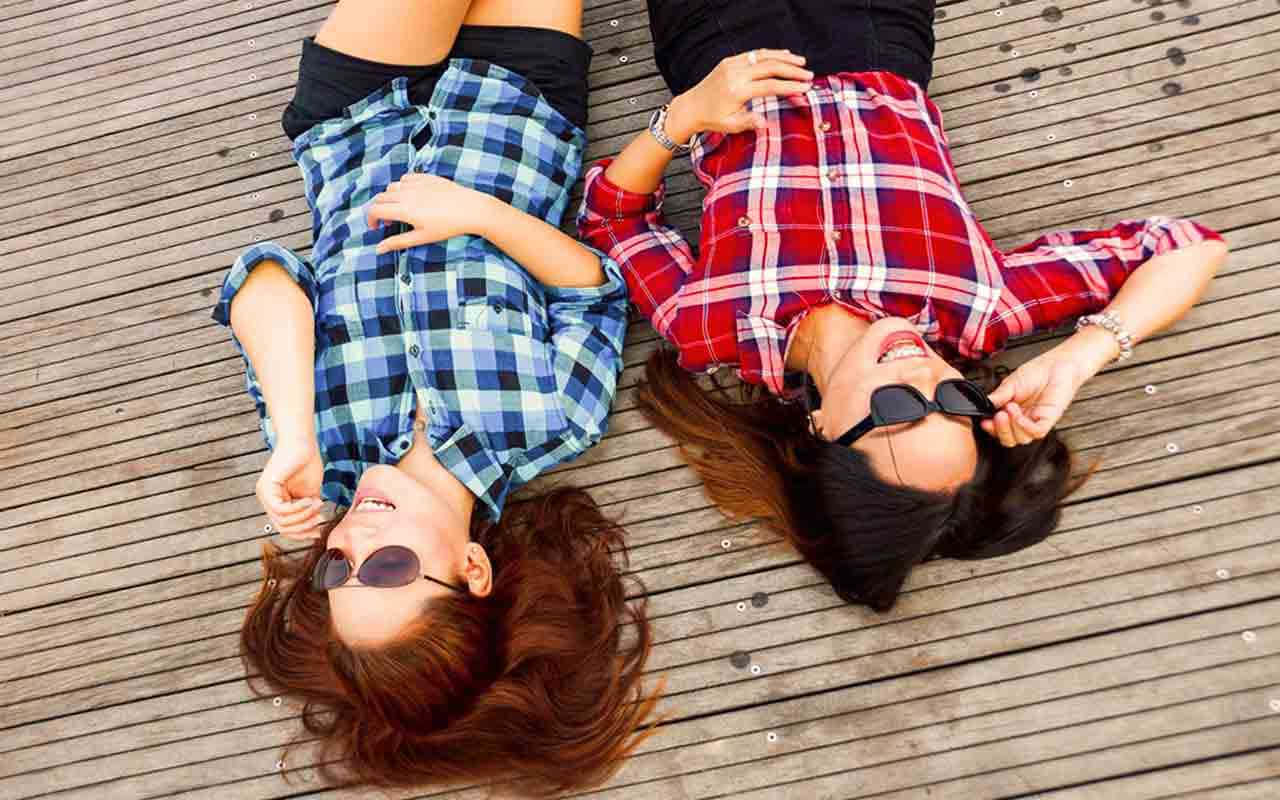 Friendship 桌布 壁紙 — 兩位微笑的女性穿著格紋襯衫躺在木甲板上，戴著太陽眼鏡大笑。