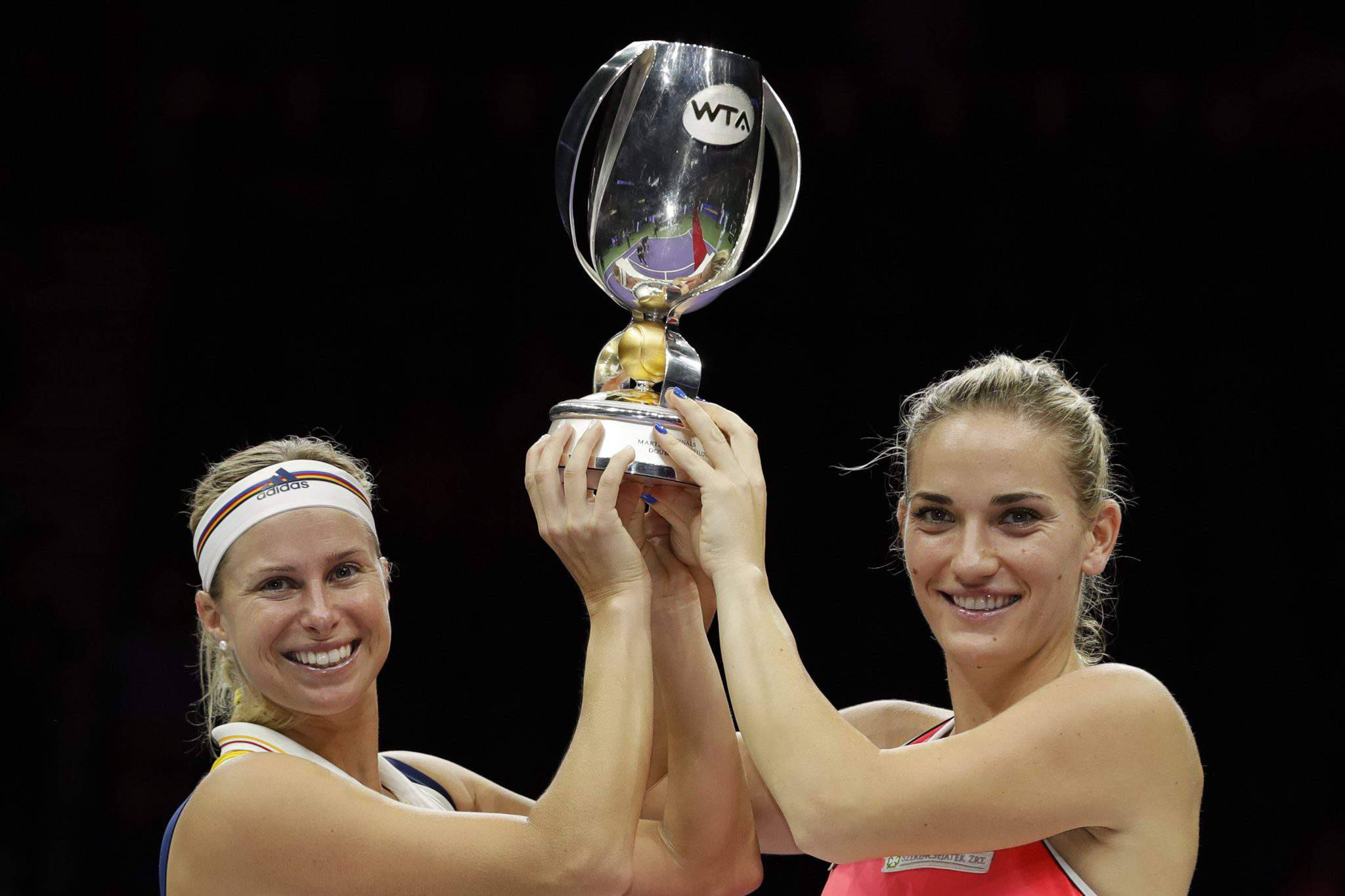 Trophy 桌布 壁紙 — 兩位微笑的女性網球選手在深色背景前共同舉起閃亮的WTA冠軍獎盃。