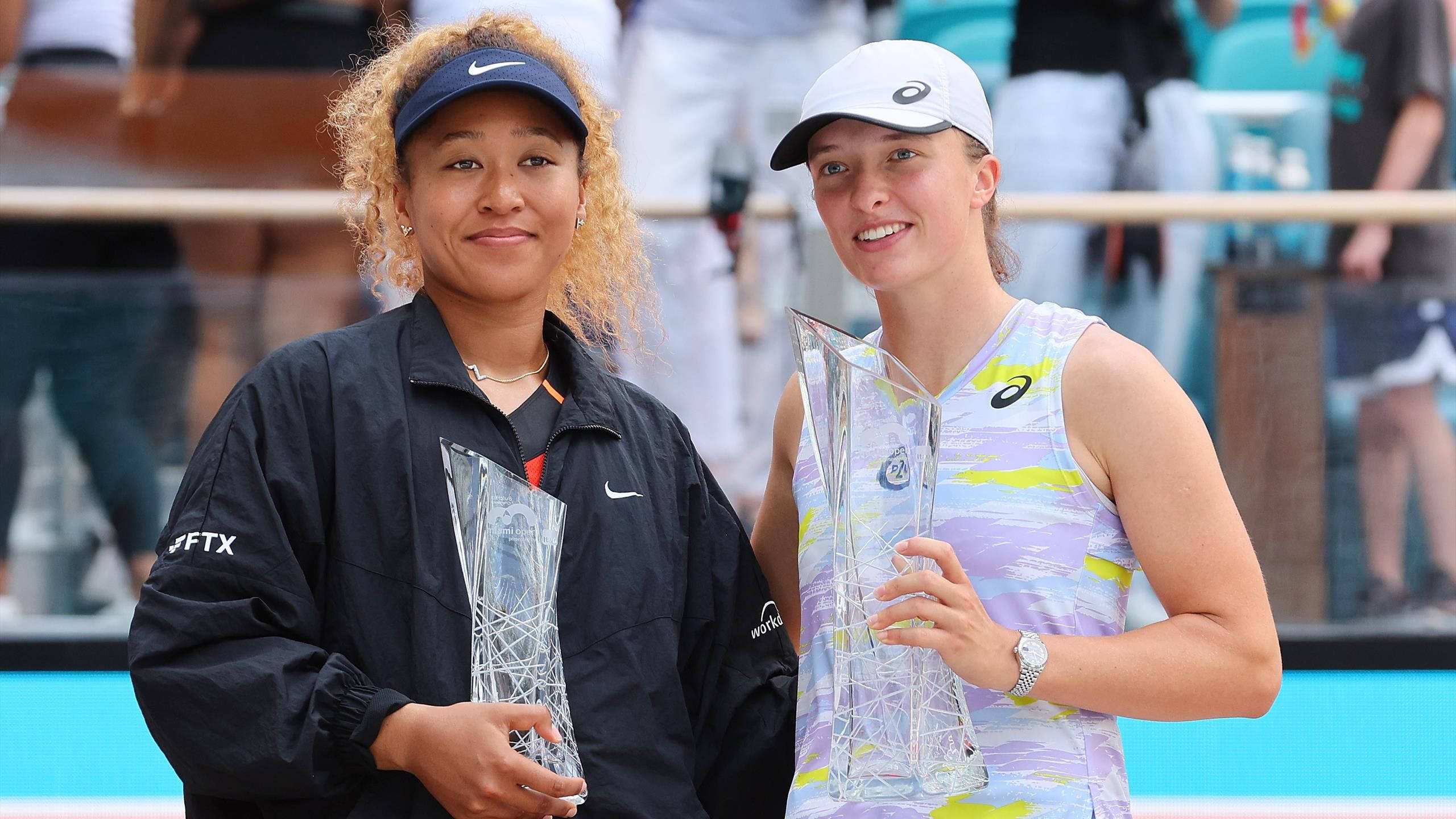 Tennis 桌布 壁紙 — 兩位微笑的女性網球選手在陽光明媚的球場上與獎盃合影，背景有觀眾。