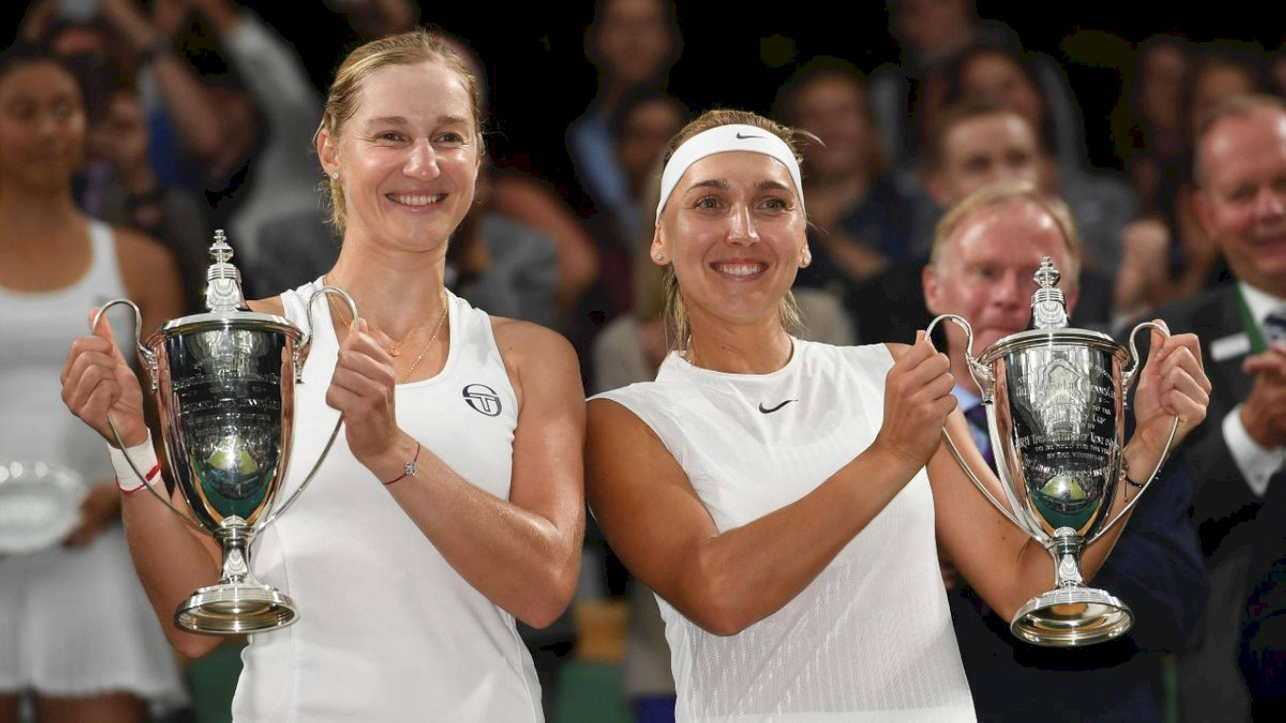 Tennis 桌布 壁紙 — 兩位微笑的女網球運動員在球場上自豪地高舉閃亮的銀色獎盃，身後是模糊的觀眾。