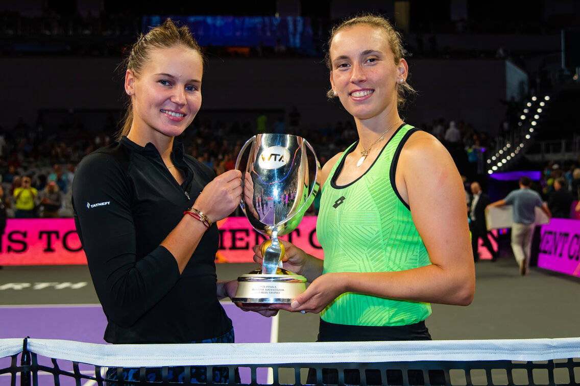 Trophy 桌布 壁紙 — 兩位微笑的女網球選手在球場上自豪地舉起閃閃發光的銀色獎盃，背景有觀眾。