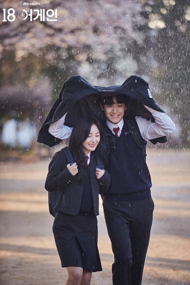 Couple 桌布 壁紙 — 兩位微笑的學生共享一件外套，在飄落的雨中遮擋，背景是柔焦的櫻花。