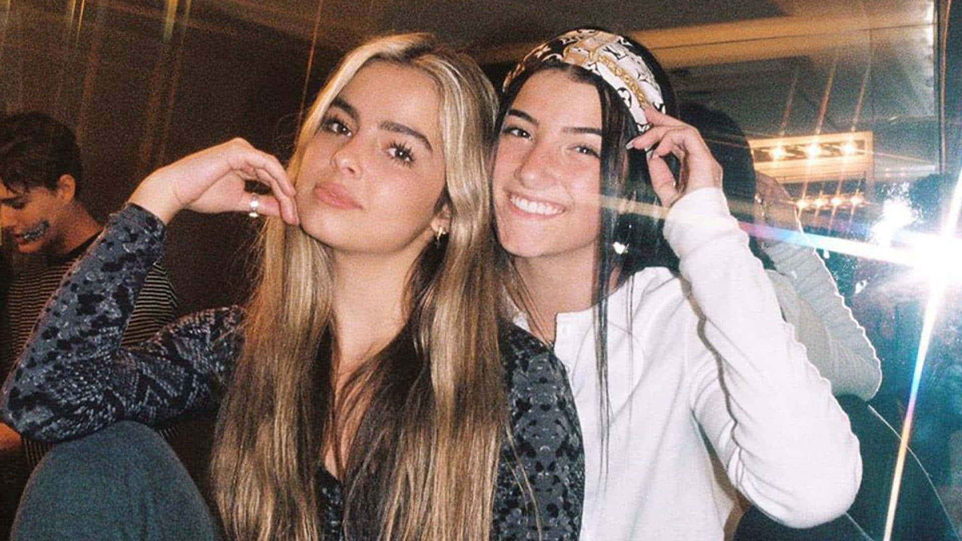 Charli And Addison 桌布 壁紙 — 兩位微笑的年輕女性在燈光昏暗的俱樂部中緊密地擺姿勢，帶有鏡頭光暈和充滿活力的背景燈光。