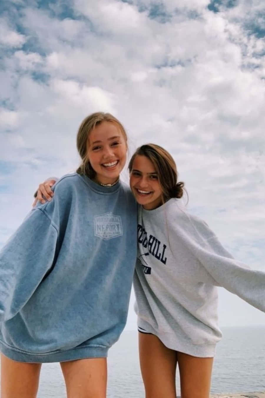 Friends 桌布 壁紙 — 兩位微笑的年輕女性穿著寬鬆毛衣在陰天海邊擁抱。