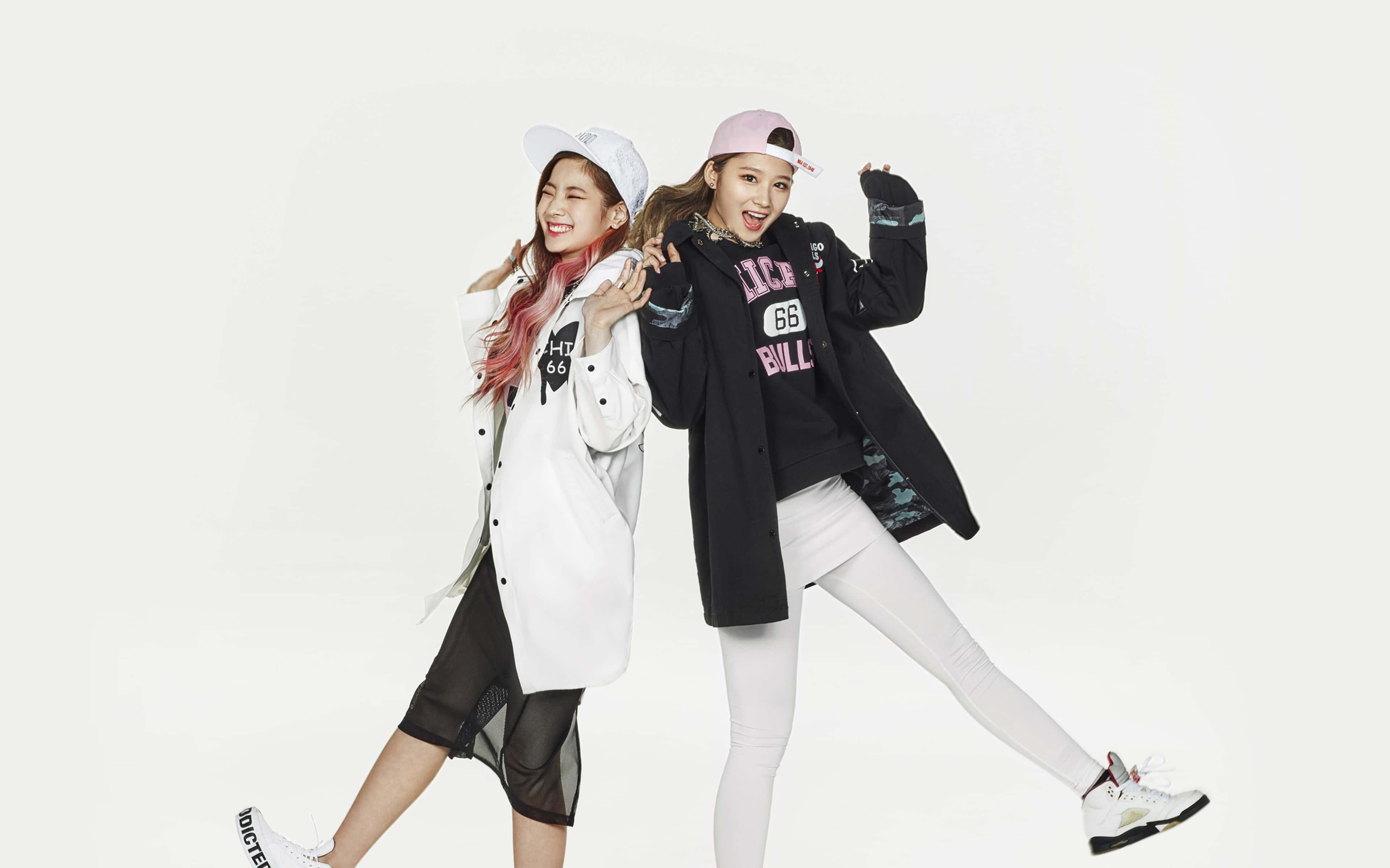 Cute Kpop 桌布 壁紙 — 兩位微笑的年輕女性穿著時尚街頭服飾，在純白背景前擺出俏皮姿勢。