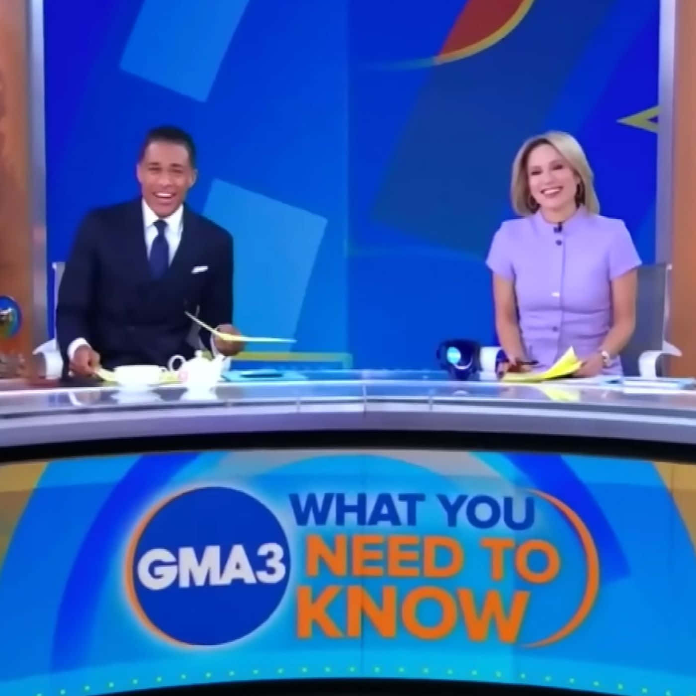 smiling 桌布 壁紙 — 兩位微笑的新聞主播坐在一張弧形桌子前，桌子帶有 'GMA3 WHAT YOU NEED TO KNOW' 品牌標誌，背景是藍色幾何圖案。