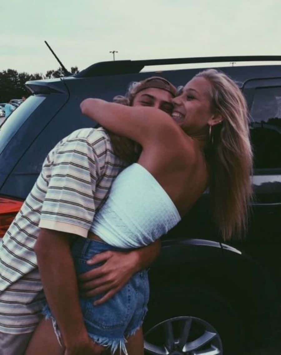 boyfriend 桌布 壁紙 — 兩位微笑的朋友在停車場一輛深色SUV旁，在柔和晚光下溫暖擁抱。