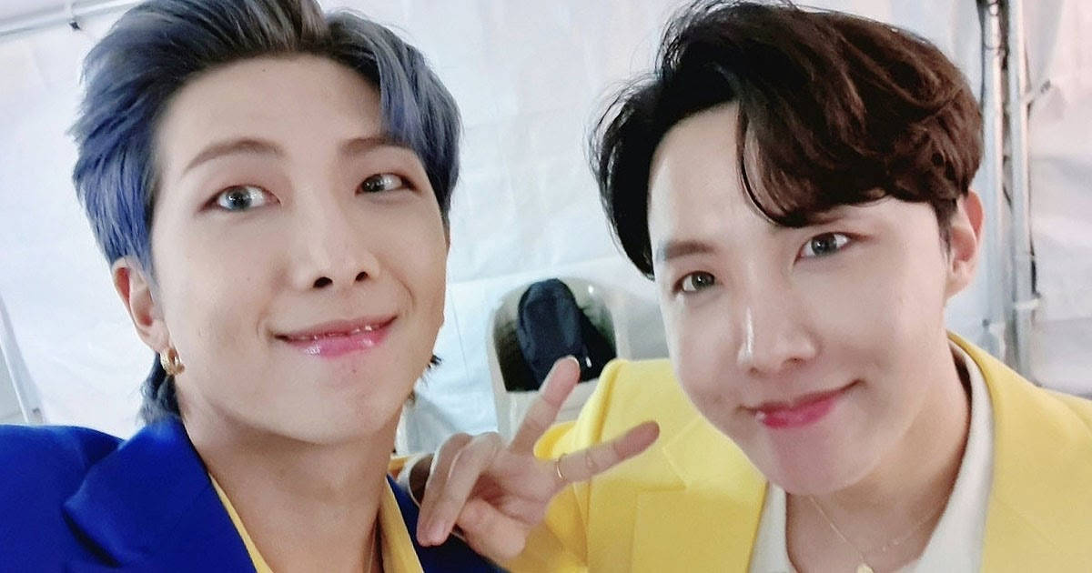 jhope 桌布 壁紙 — 兩位微笑的男士，一頭藍色和棕色頭髮，在明亮的室內環境中緊密擺姿勢，其中一人做出和平手勢。
