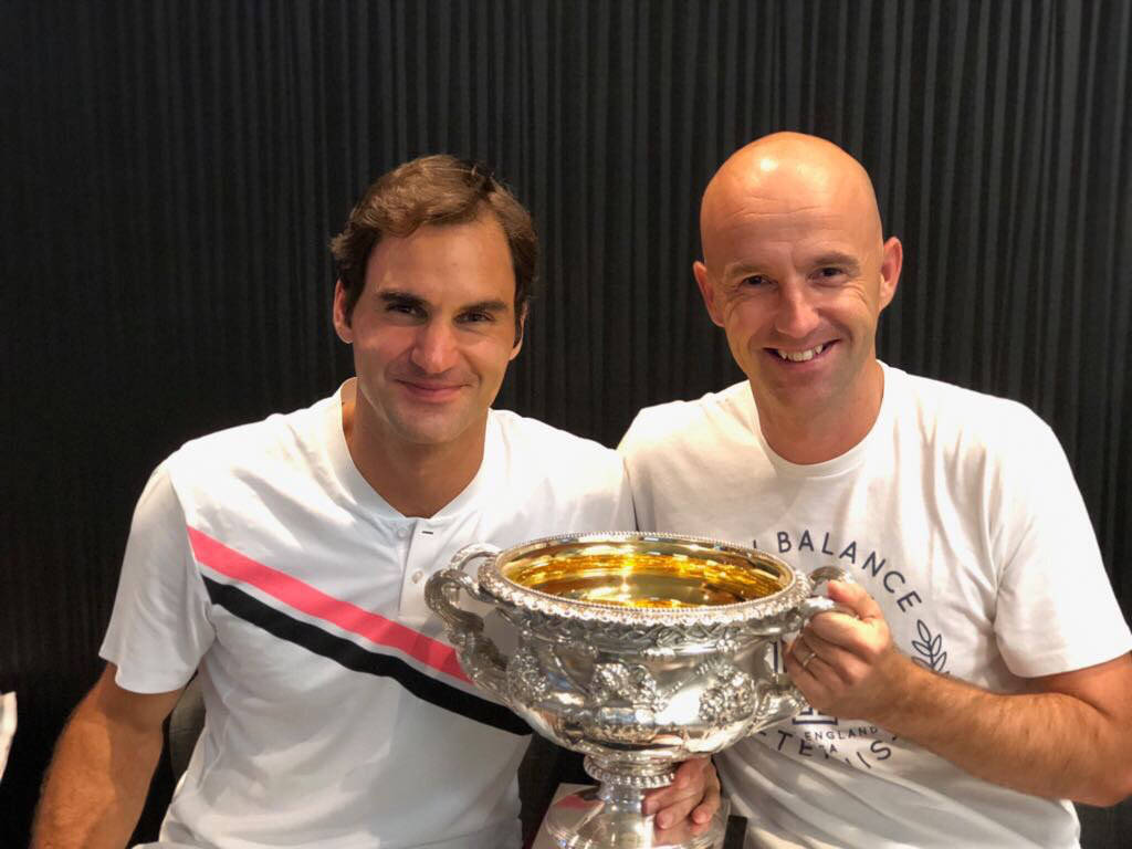 Tennis 桌布 壁紙 — 兩位微笑的男士在深色垂直條紋背景前，手持一個大型華麗銀色獎盃擺姿勢。