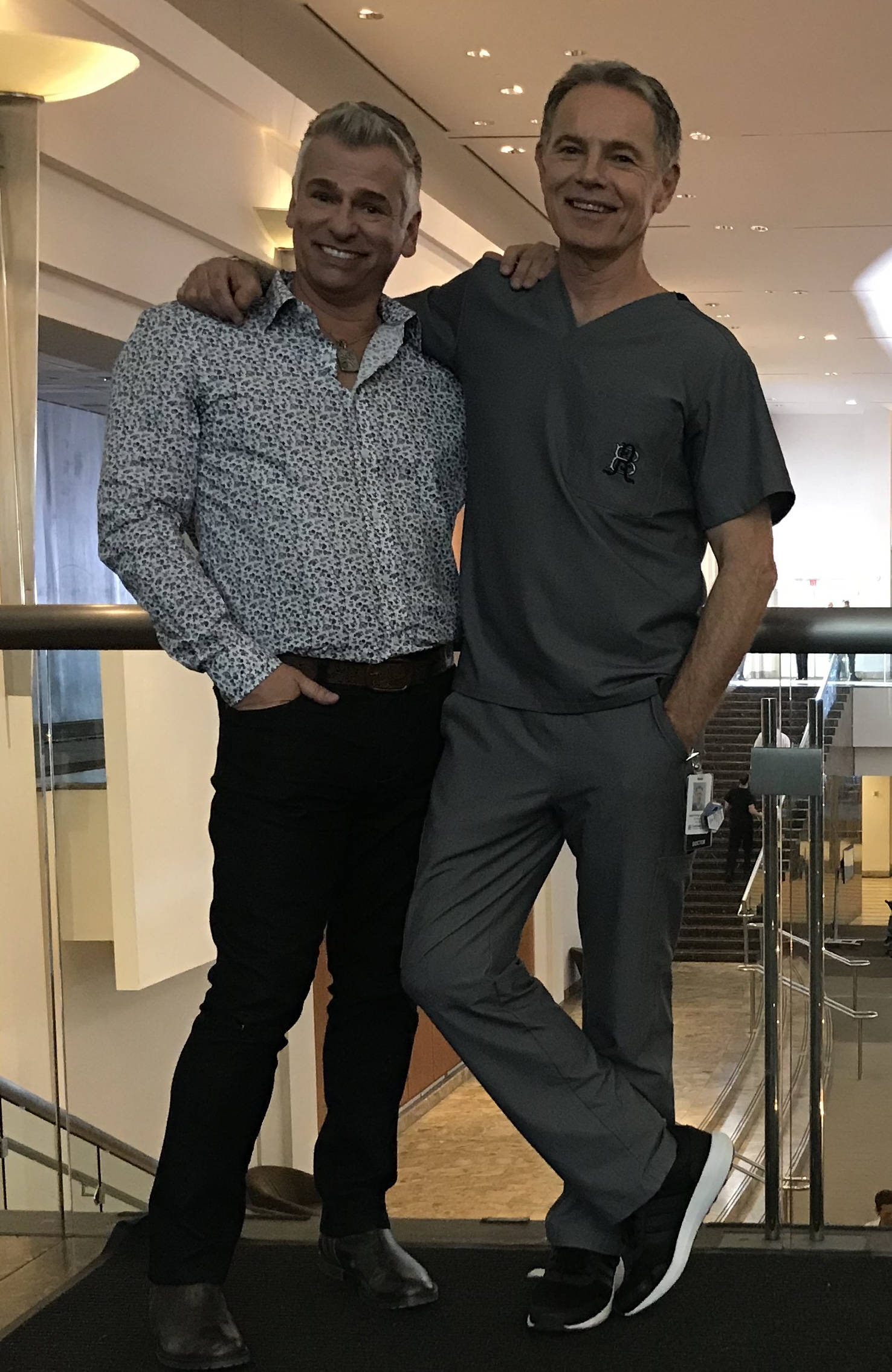 Smile 桌布 壁紙 — 兩位微笑的男子在一個現代化的室內陽台上合影，陽台配有玻璃欄杆和溫暖的頭頂燈光。