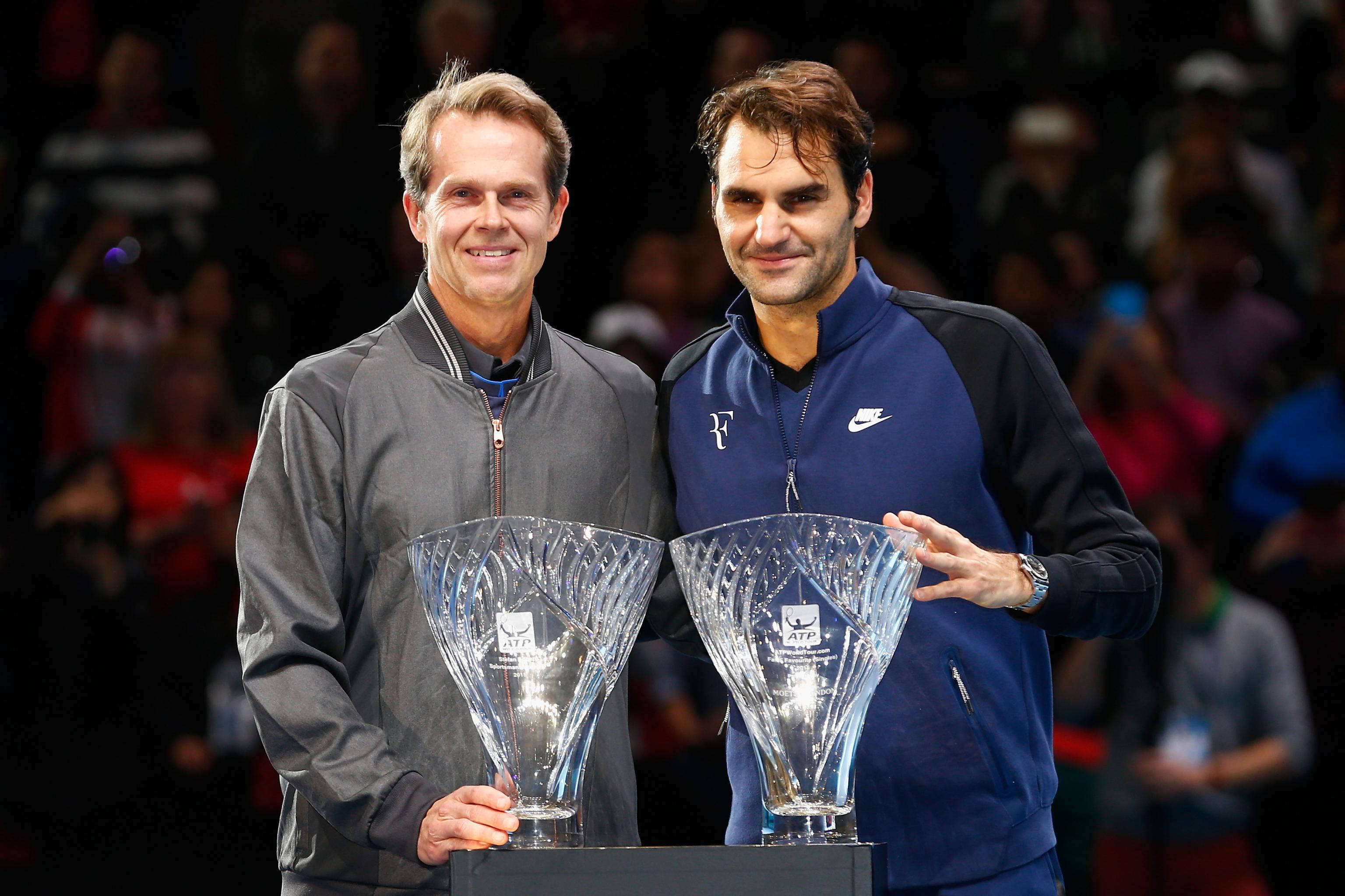 Tennis 桌布 壁紙 — 兩位微笑的網球傳奇並肩站立，在明亮的場館燈光下手持大型水晶獎盃。