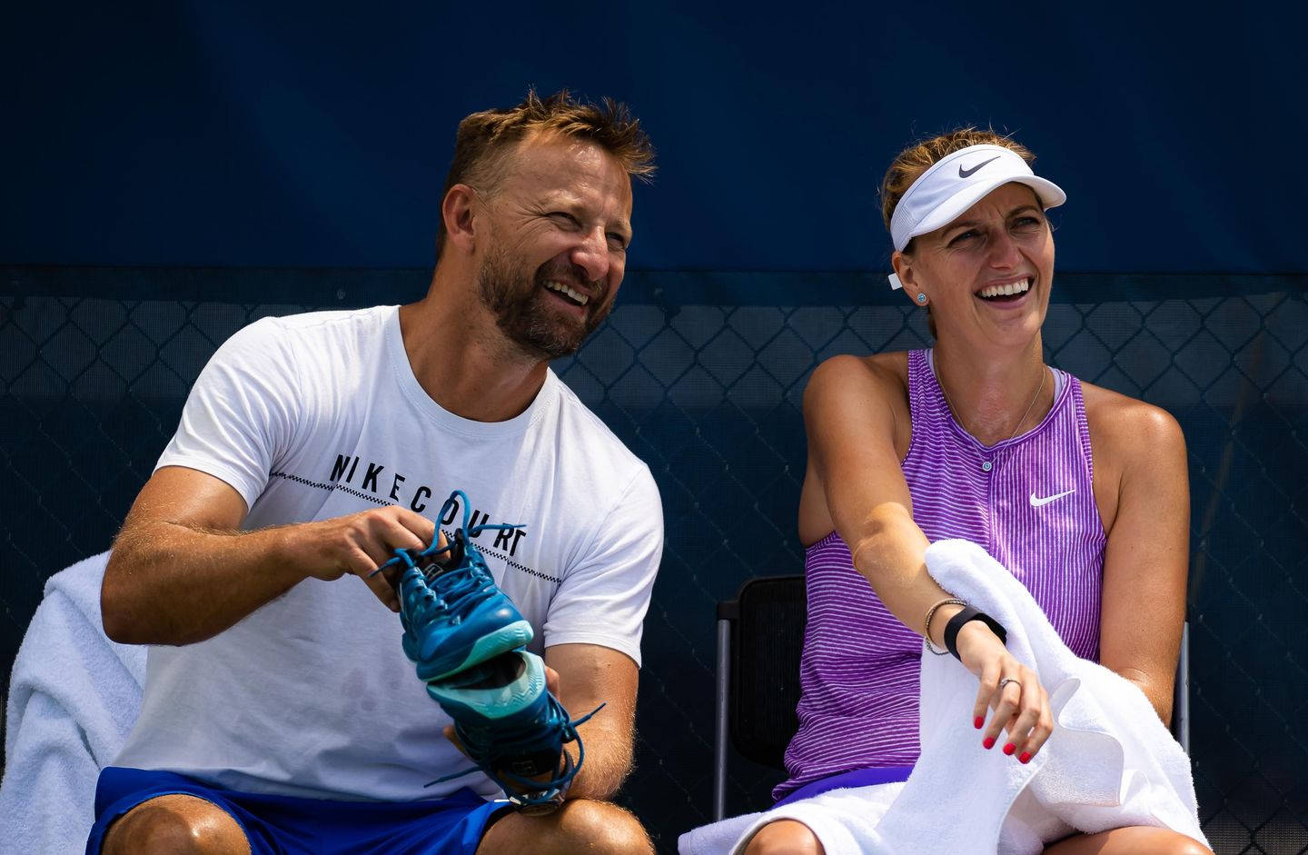 Tennis 桌布 壁紙 — 兩位微笑的網球選手在球場椅子上放鬆，一人拿著藍色鞋子，另一人膝上搭著毛巾。