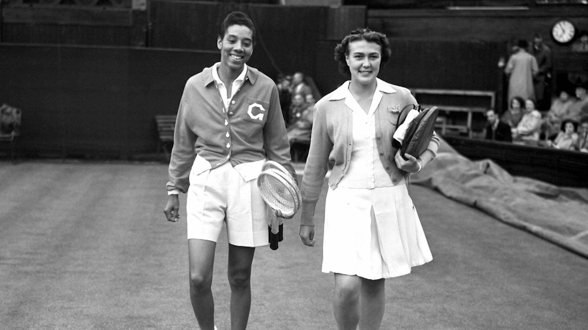 Tennis 桌布 壁紙 — 兩位微笑的網球選手穿著復古服裝，拿著球拍和袋子離開草地網球場。