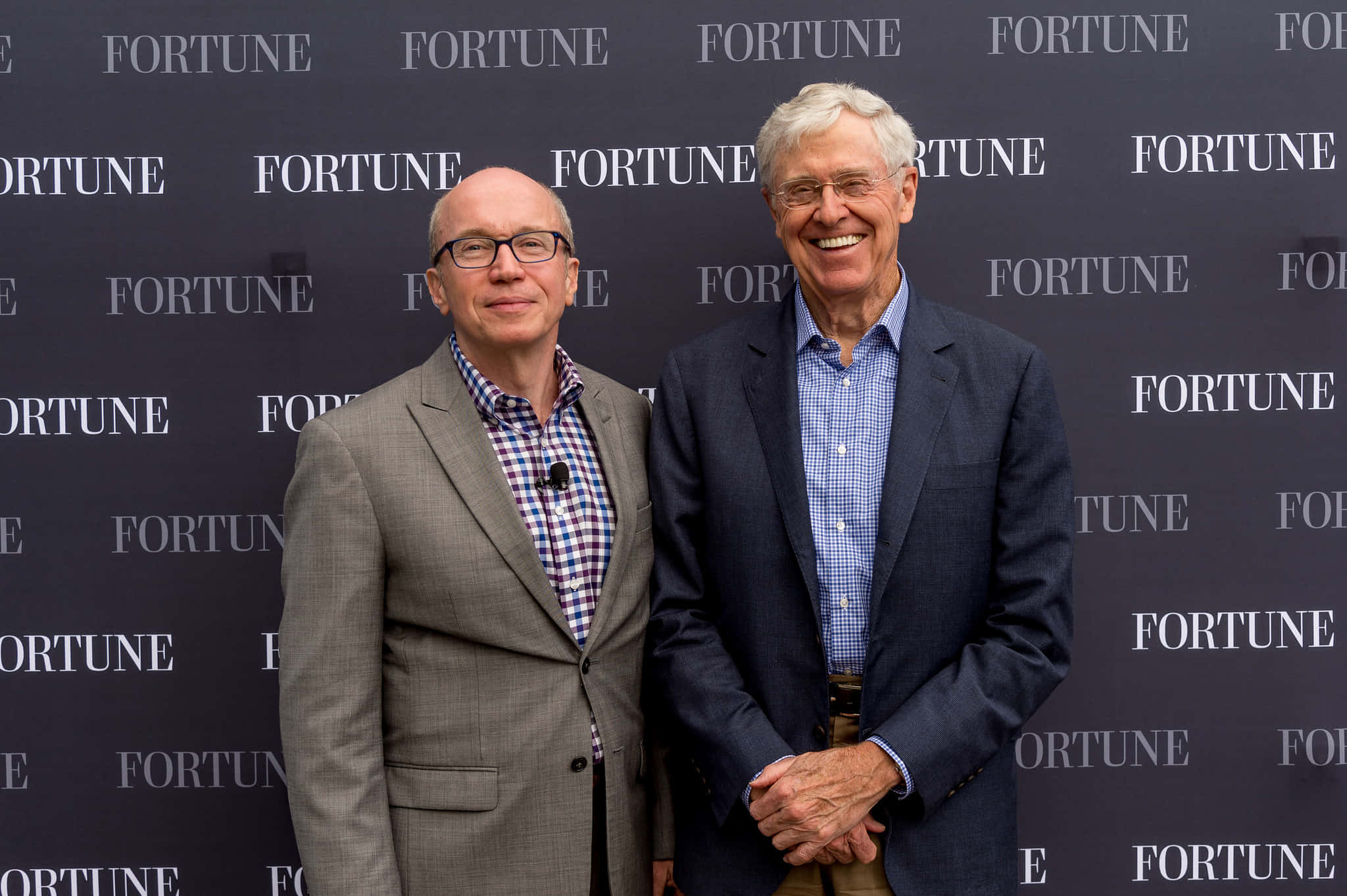smiling 桌布 壁紙 — 兩位微笑的西裝男士在正式活動中，自信地站在重複的 Fortune 標誌背景前擺姿勢。