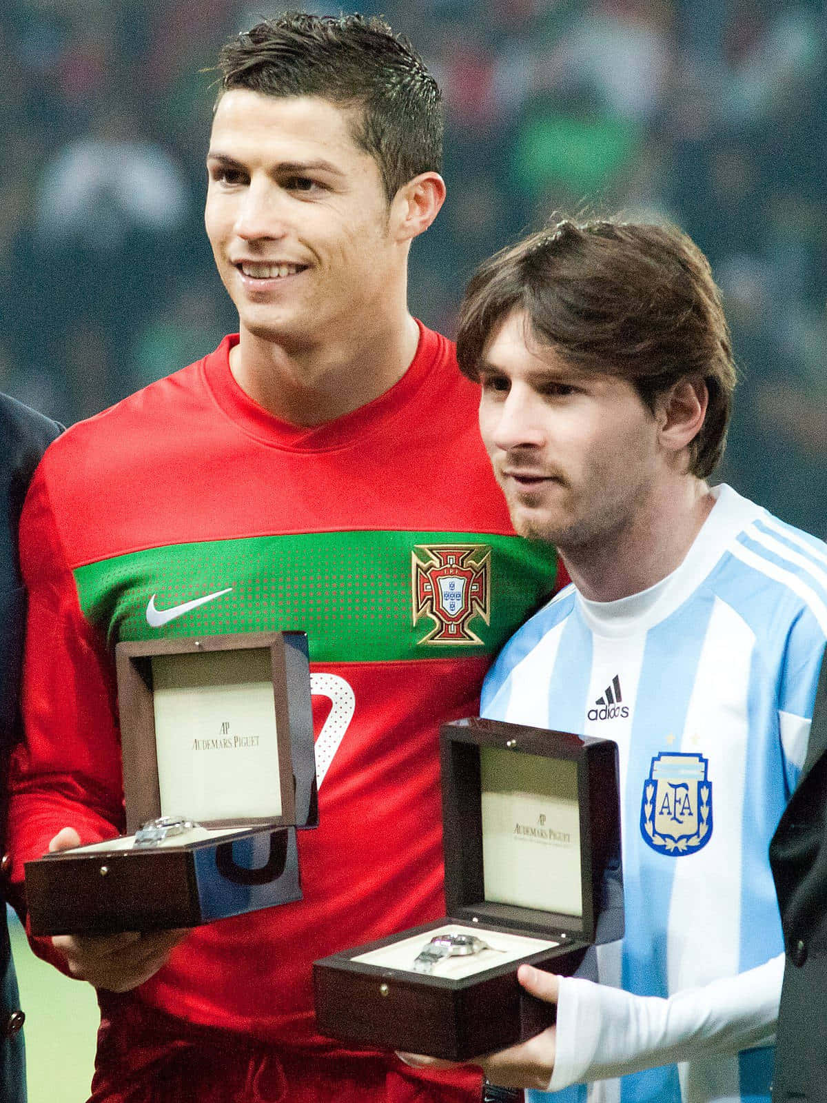 Messi And Ronaldo 4K 桌布 壁紙 — 兩位微笑的足球巨星身穿國家隊球衣，在球場上捧著打開的獎盃盒。