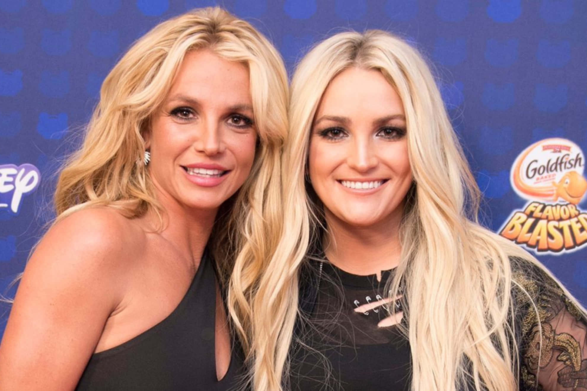 Britney Spears 桌布 壁紙 — 兩位微笑的金髮女性在Goldfish Flavor Blaster活動中，在藍色品牌背景前一起擺姿勢。