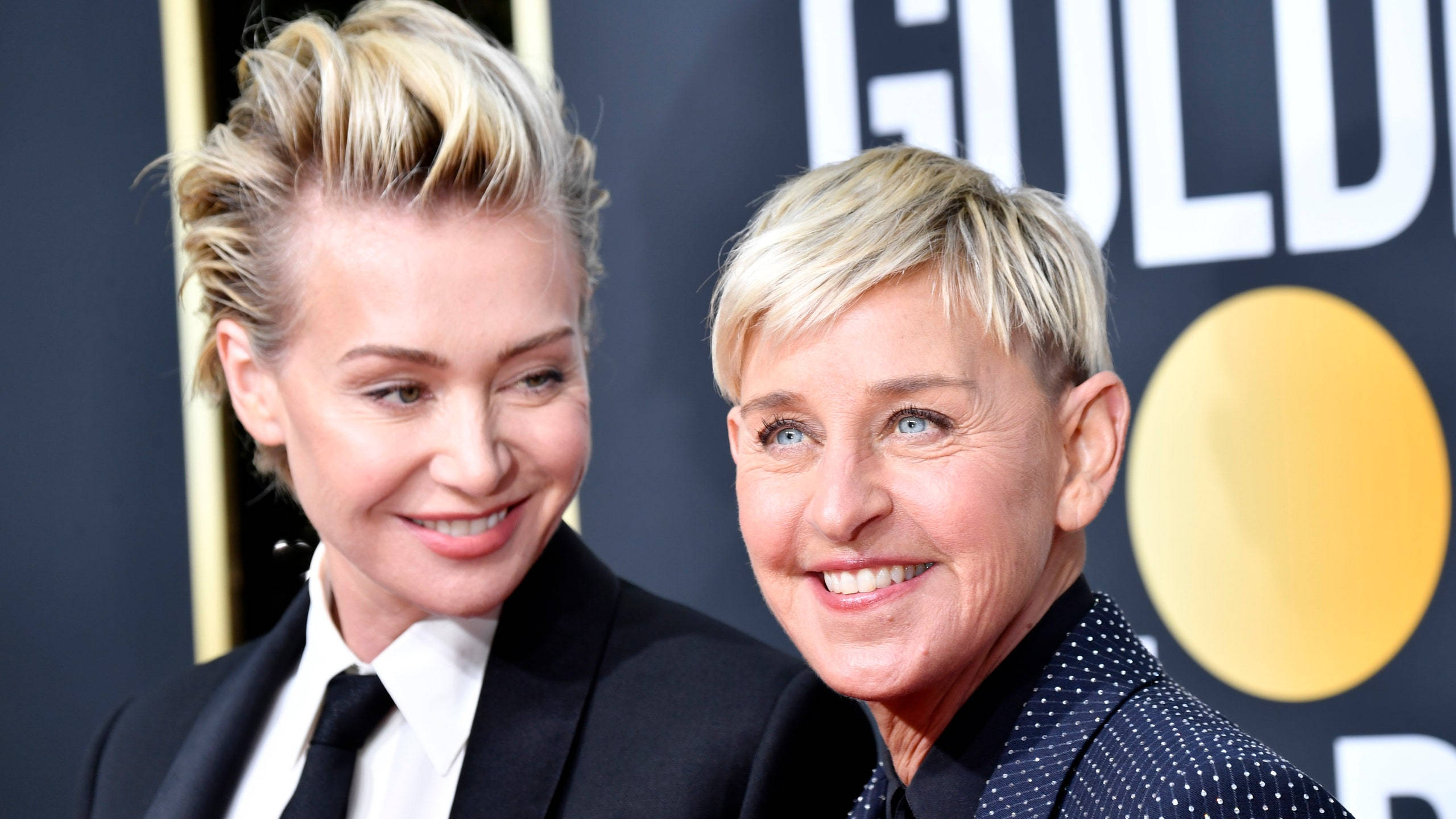 Ellen Degeneres 桌布 壁紙 — 兩位微笑的金髮女性穿著正式服裝，在金色背景的華麗頒獎典禮上一起擺姿勢。