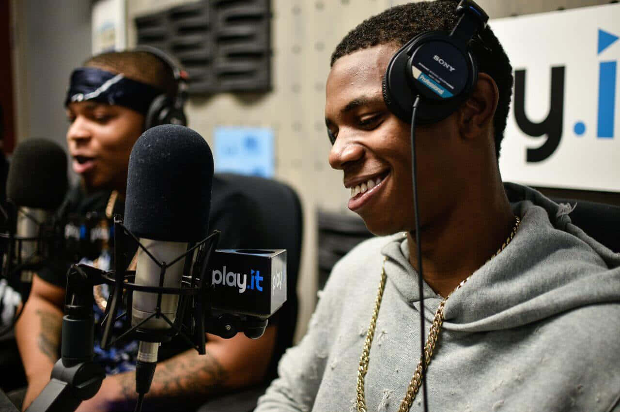 A Boogie Wit Da Hoodie 桌布 壁紙 — 兩位微笑的饒舌歌手在錄音室戴著耳機和金鏈，帶有麥克風和「play.it」品牌標誌。