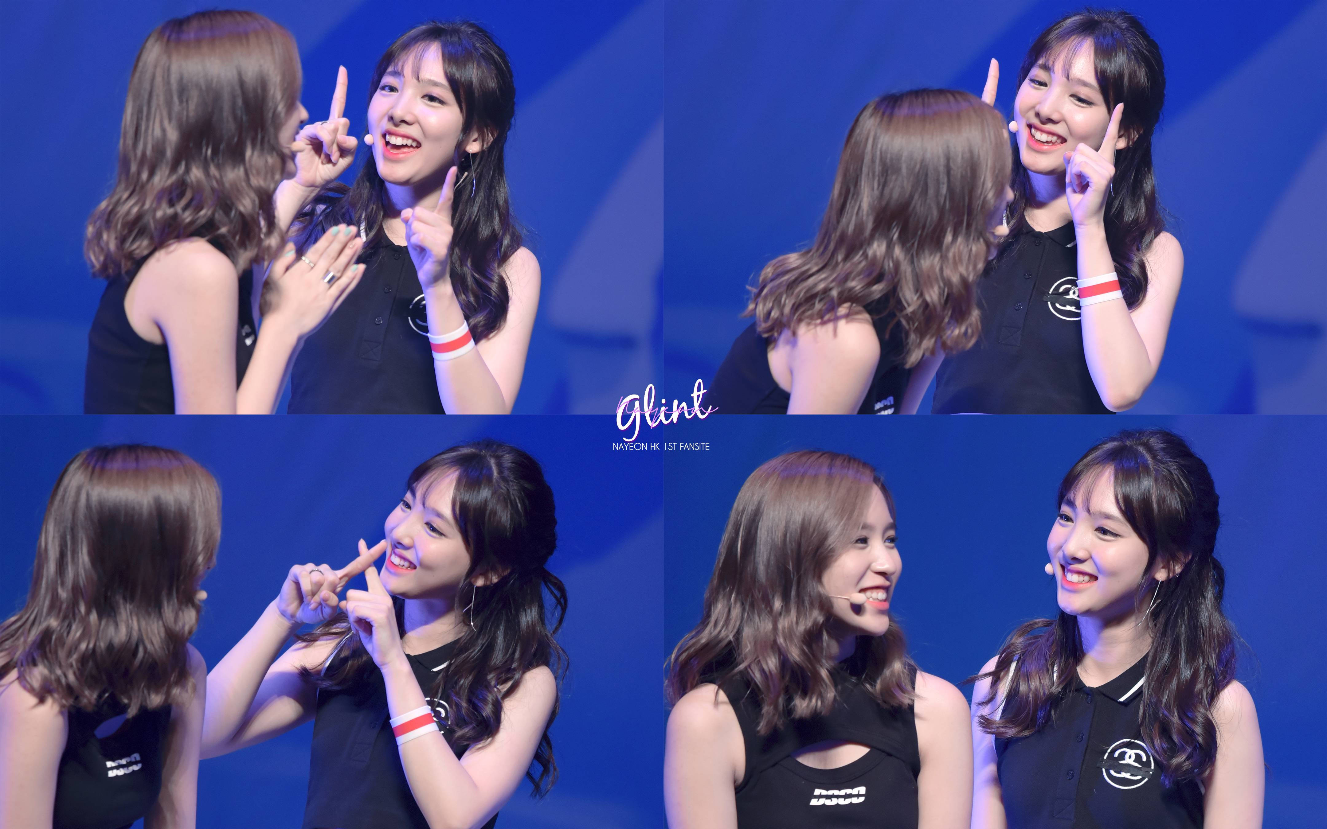 twice 桌布 壁紙 — 兩位微笑的黑上衣女性在藍色舞台上以相配的手指手勢互動玩耍。