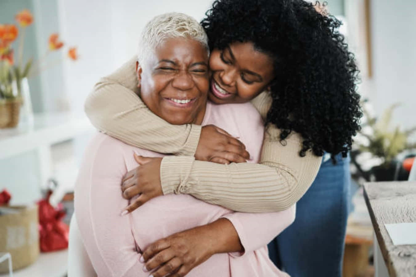 Hug 桌布 壁紙 — 兩位微笑的黑人女性在明亮的室內環境中，在柔和自然光下溫暖地擁抱。
