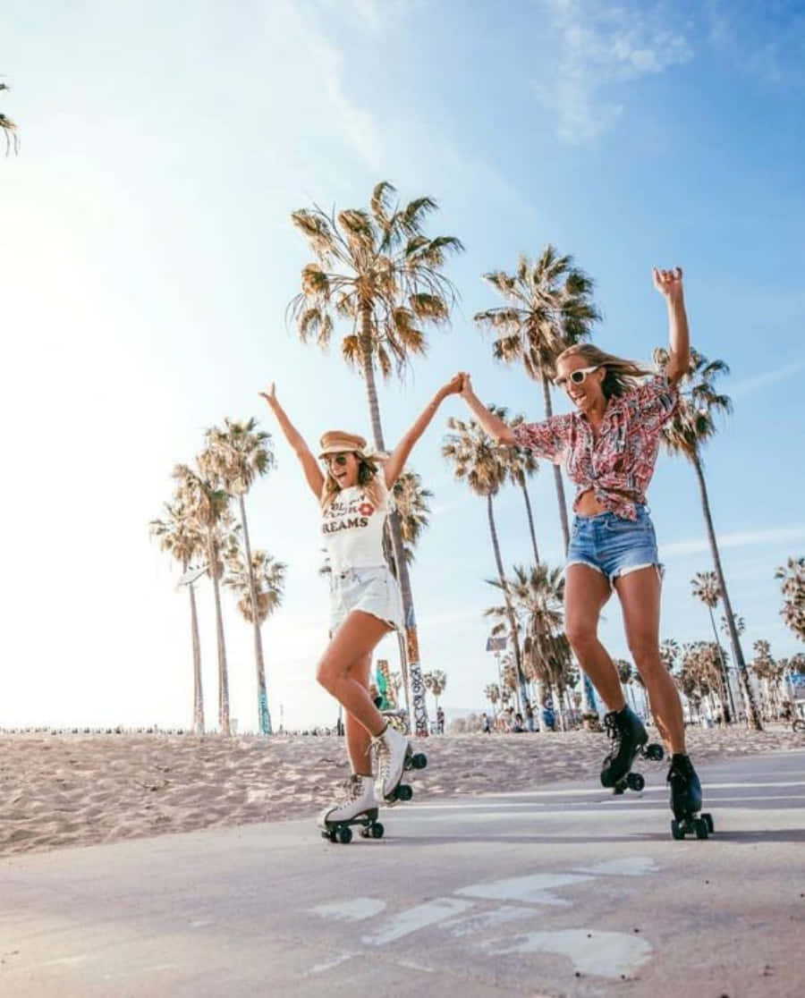 Friends 桌布 壁紙 — 兩位快樂的女性手牽手，沿著陽光明媚、棕櫚樹成行的海灘木板路溜冰。