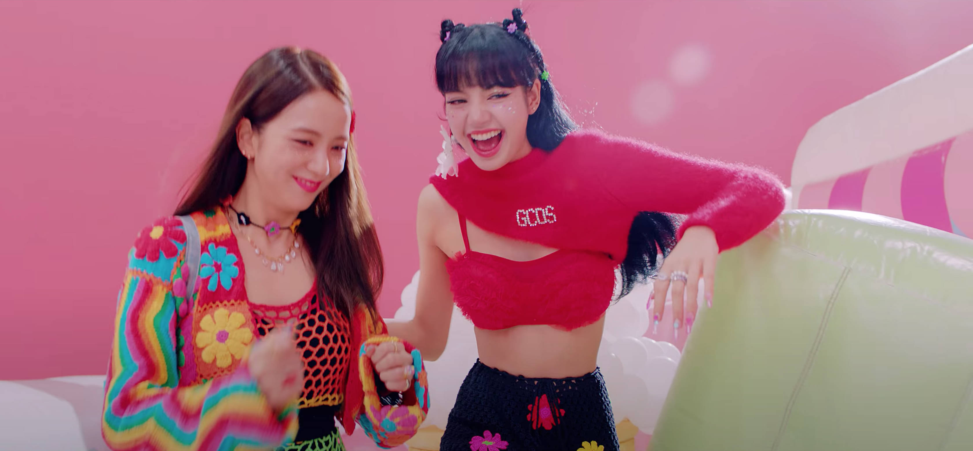 Lalisa 桌布 壁紙 — 兩位快樂的女性穿著鮮豔多彩的服裝，在明亮的粉紅色背景和充氣道具前一起大笑。