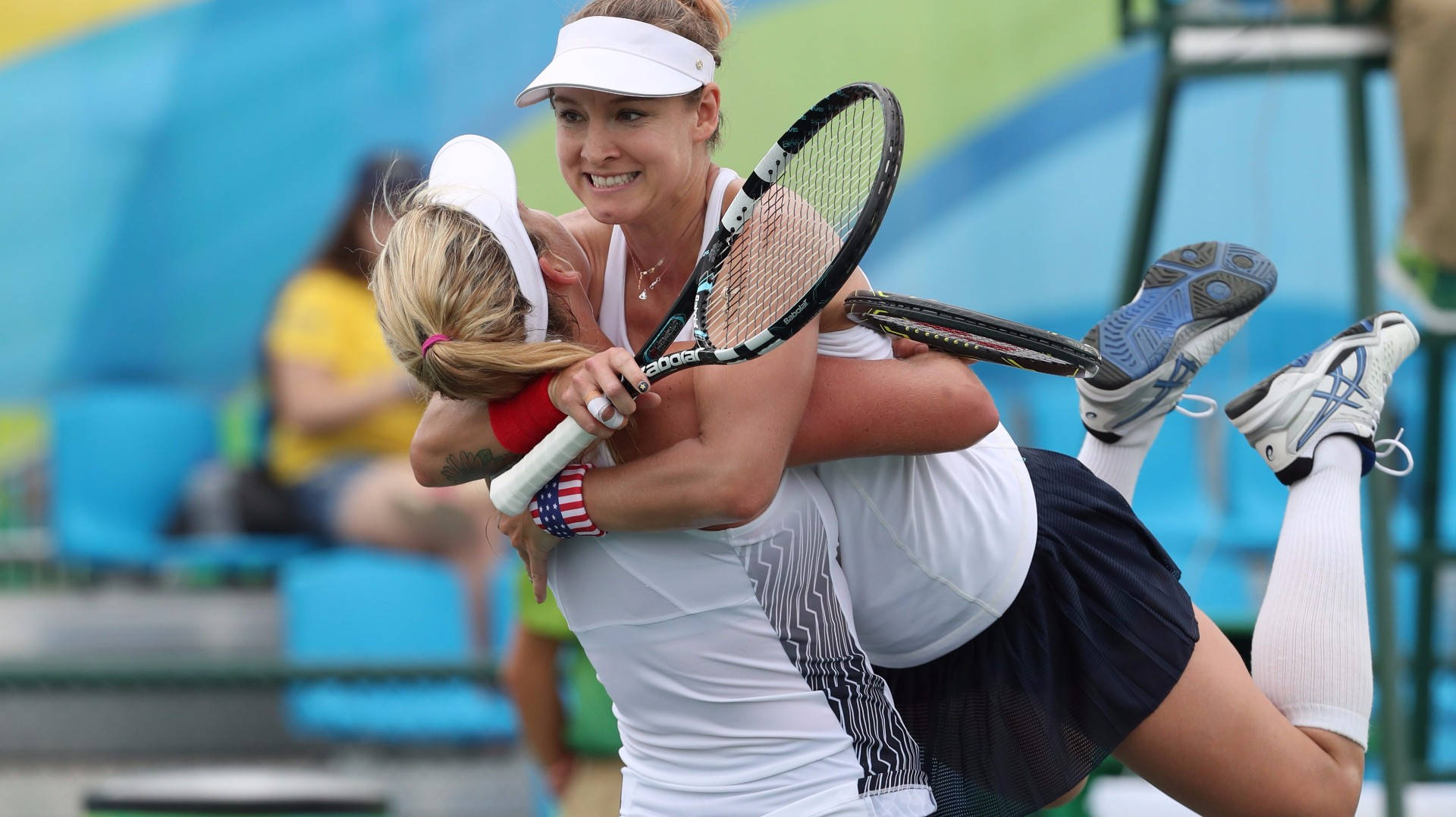 Tennis 桌布 壁紙 — 兩位快樂的女網球選手在明亮的球場上手持球拍在半空中擁抱，慶祝勝利。