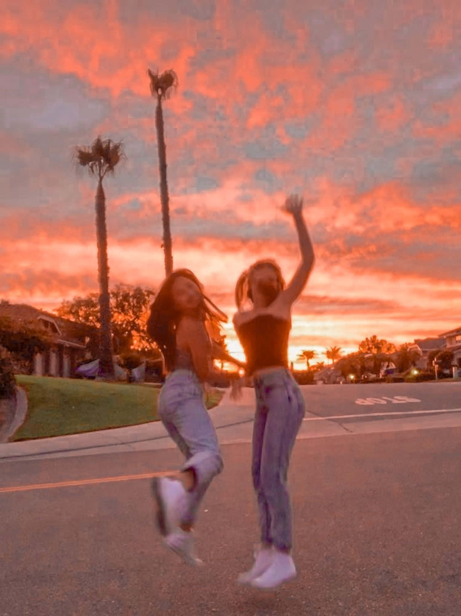 Friends 桌布 壁紙 — 兩位快樂的朋友在郊區街道上躍起，背景是火紅的橙色和粉紅色日落天空。