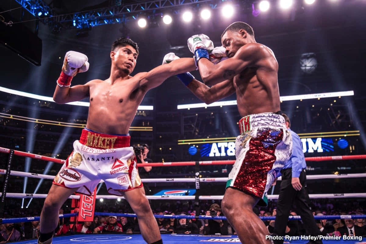 Boxing 桌布 壁紙 — 兩位拳擊手在燈光明亮的擂台上交鋒，其中一人在激烈的職業比賽中向對手擊出強力一拳。