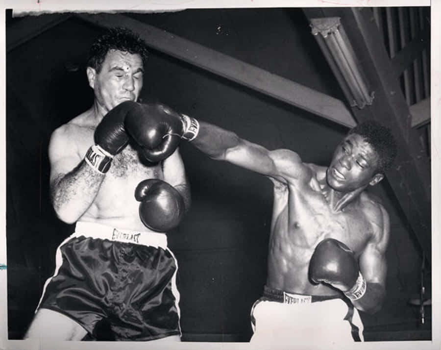 Boxing 桌布 壁紙 — 兩位拳擊手在粗糙的黑白健身房中交鋒，其中一人向另一人揮出強力一拳。