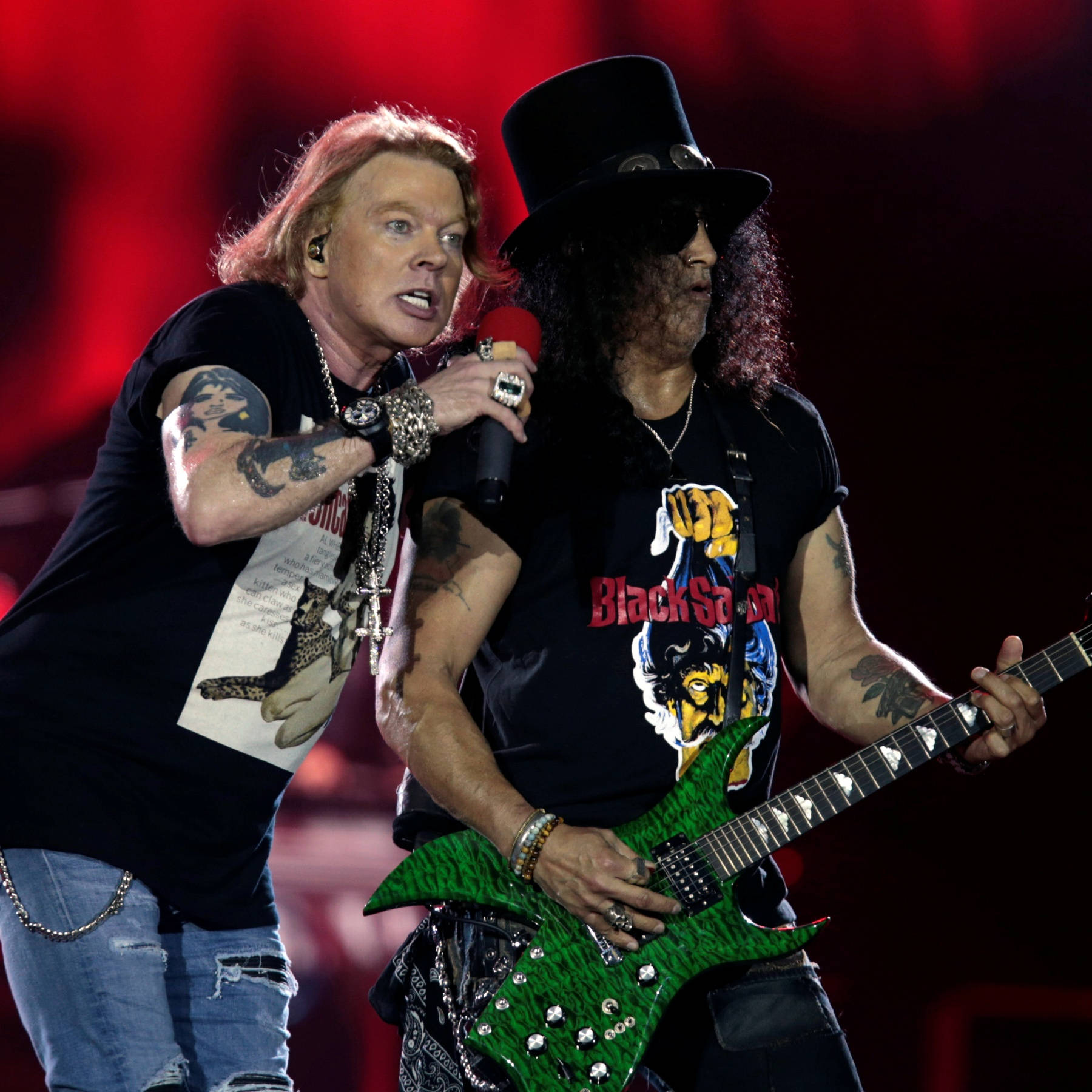 guns n roses 桌布 壁紙 — 兩位搖滾音樂家在舞台上表演，一位對著麥克風唱歌，另一位在紅燈下彈奏綠色電吉他。