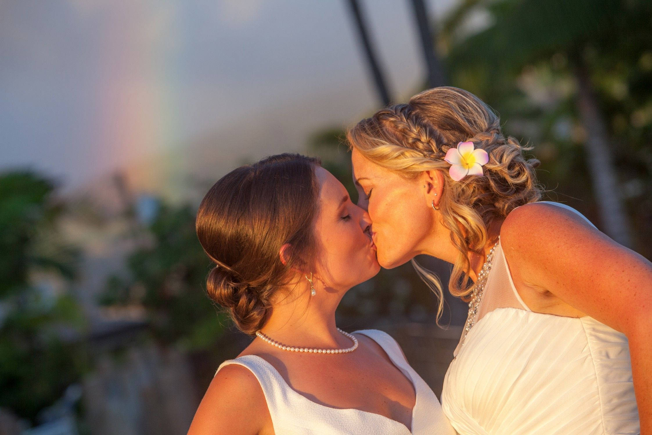 lesbians 桌布 壁紙 — 兩位新娘在柔和的彩虹下溫柔親吻，金色夕陽灑滿她們的白色婚紗。