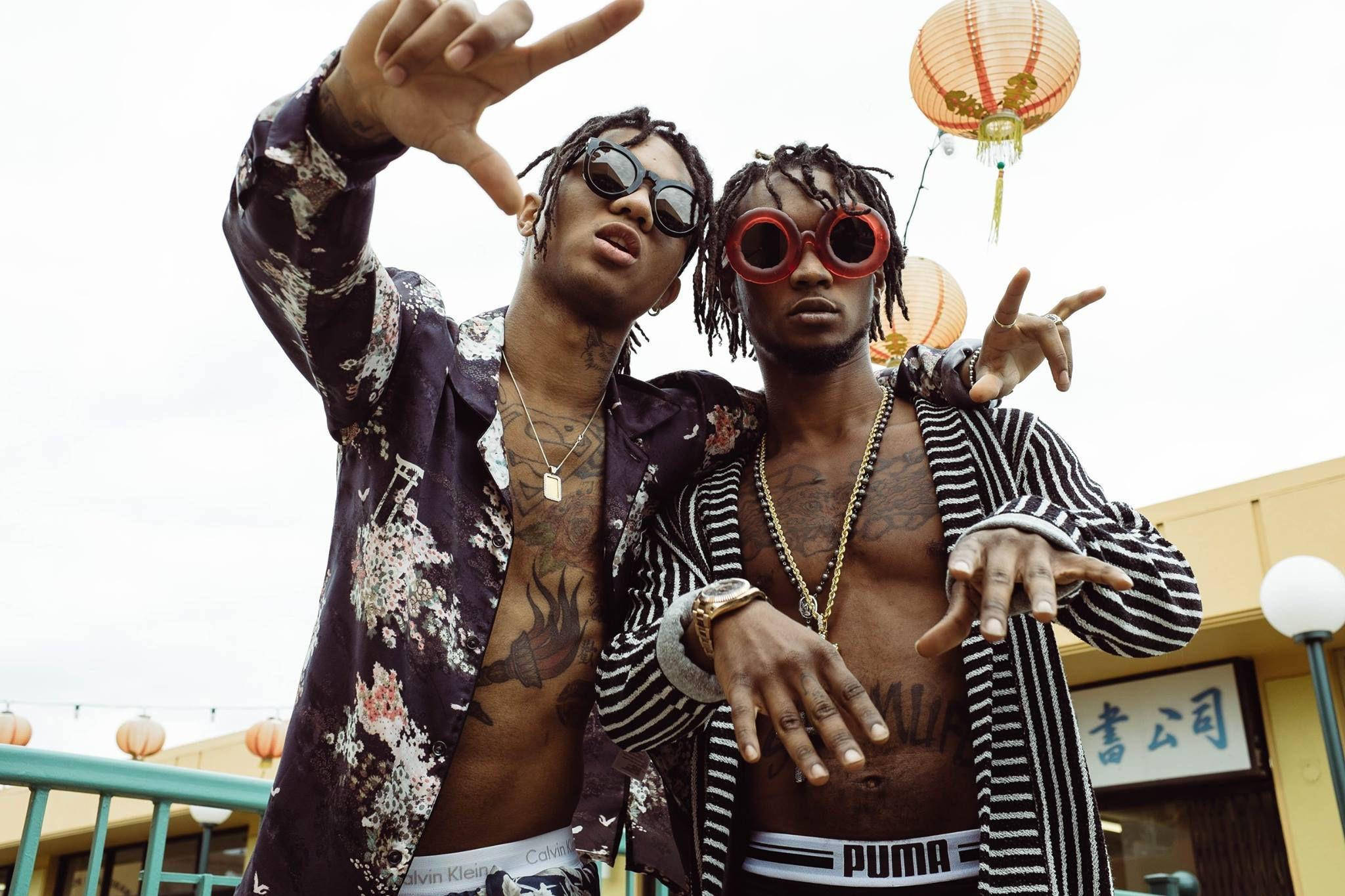 Swae Lee 桌布 壁紙 — 兩位時尚刺青男士戴著大膽太陽眼鏡和開襟外套，自信地在懸掛的紙燈籠下擺姿勢。