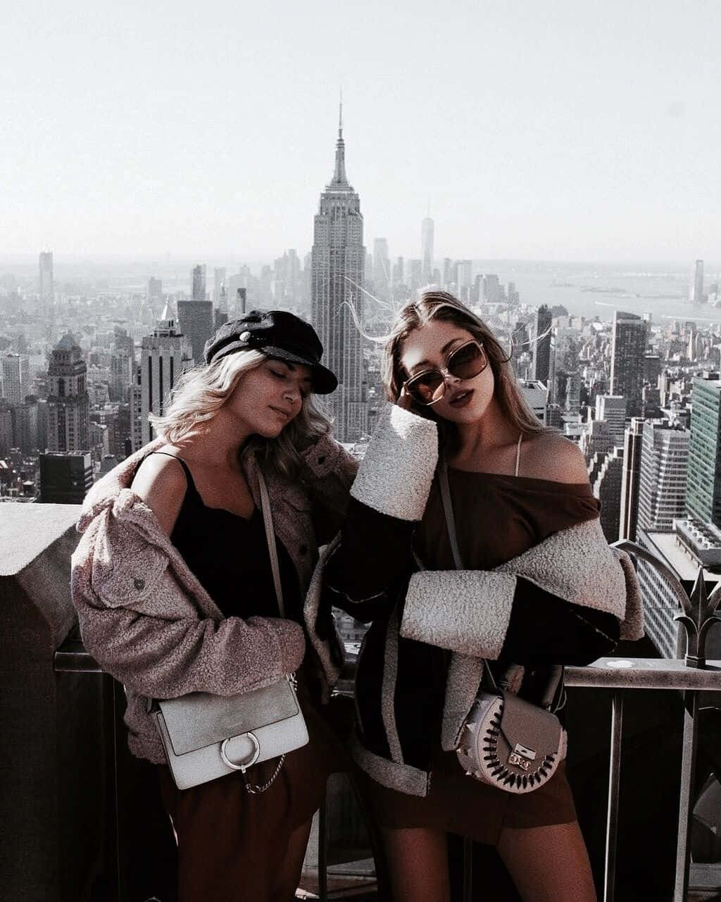 Best Friend Aesthetic 桌布 壁紙 — 兩位時尚女性在屋頂上擺姿勢，俯瞰著標誌性的紐約市天際線，帝國大廈盡收眼底。