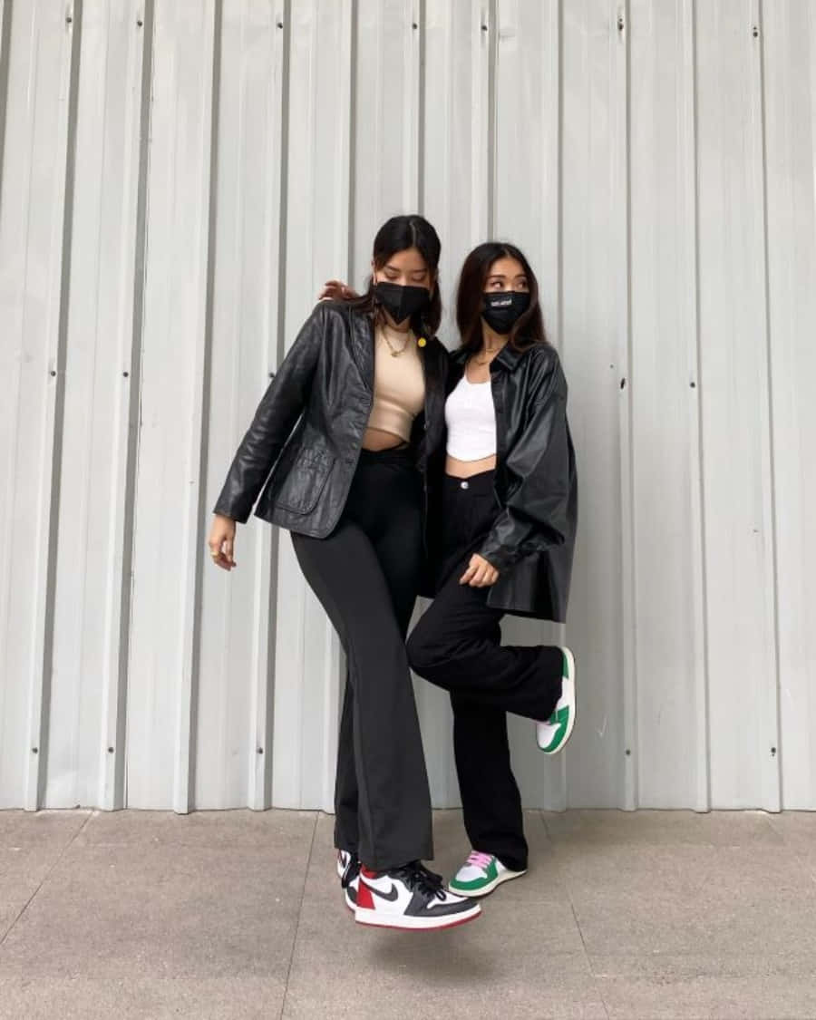 摯友 桌布 壁紙 — 兩位時尚女性穿著黑色皮夾克和口罩，在波紋金屬牆前俏皮地擺姿勢。