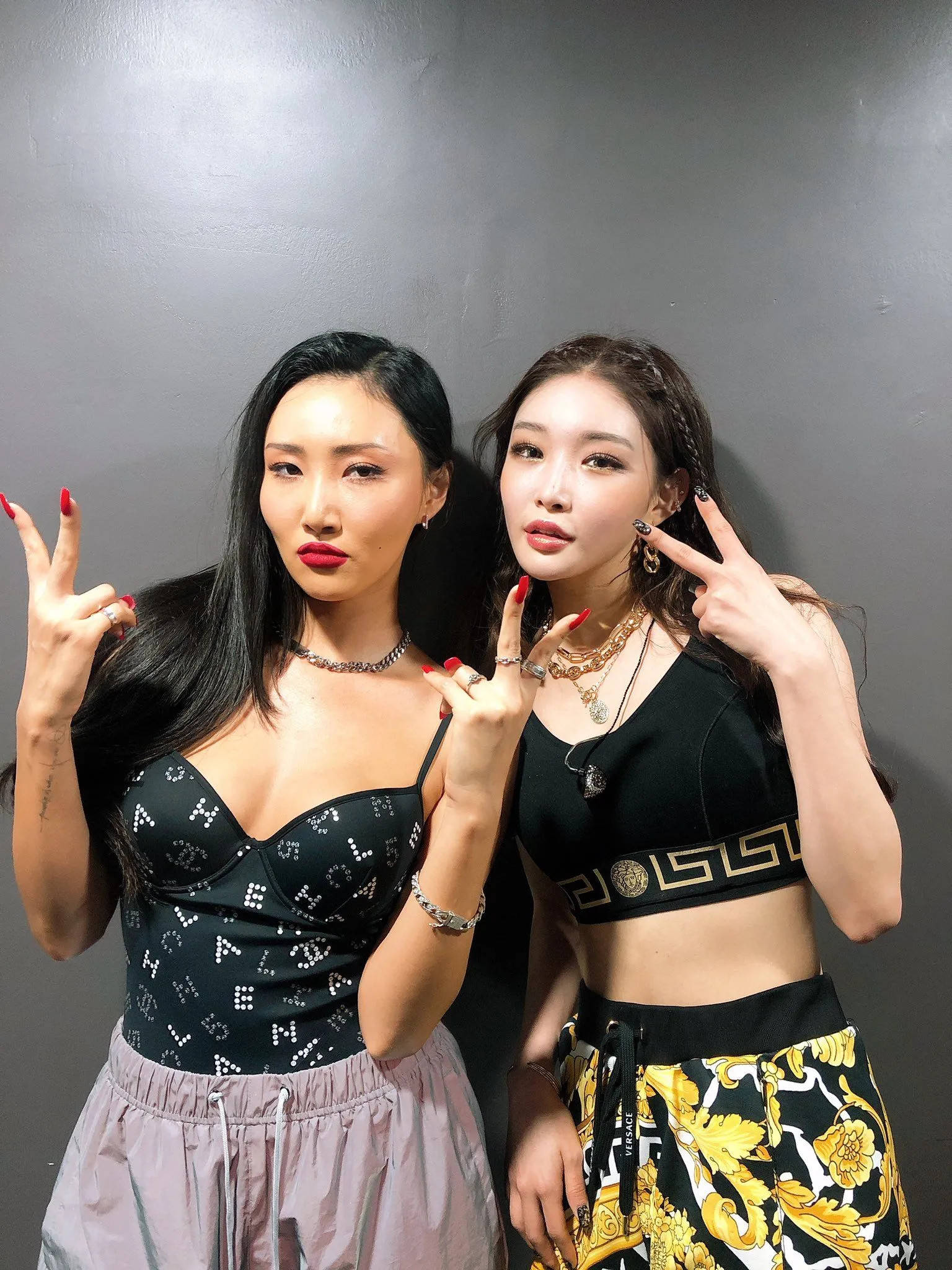 Chungha 桌布 壁紙 — 兩位時尚女性自信地靠在純灰色牆壁上擺姿勢，用紅色指甲油做出和平手勢。