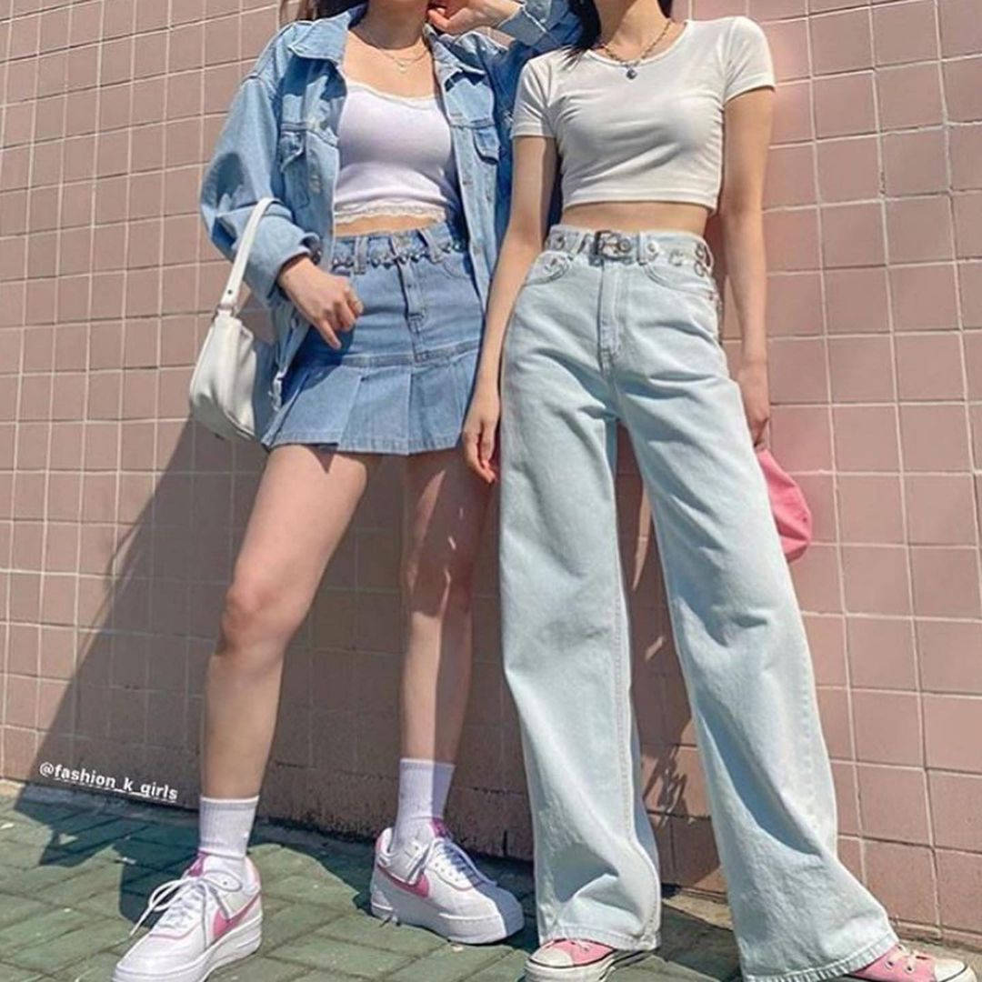Denim 桌布 壁紙 — 兩位時尚年輕女性在陽光下穿著時尚牛仔服飾和粉紅色運動鞋，在粉紅色瓷磚牆前擺姿勢。