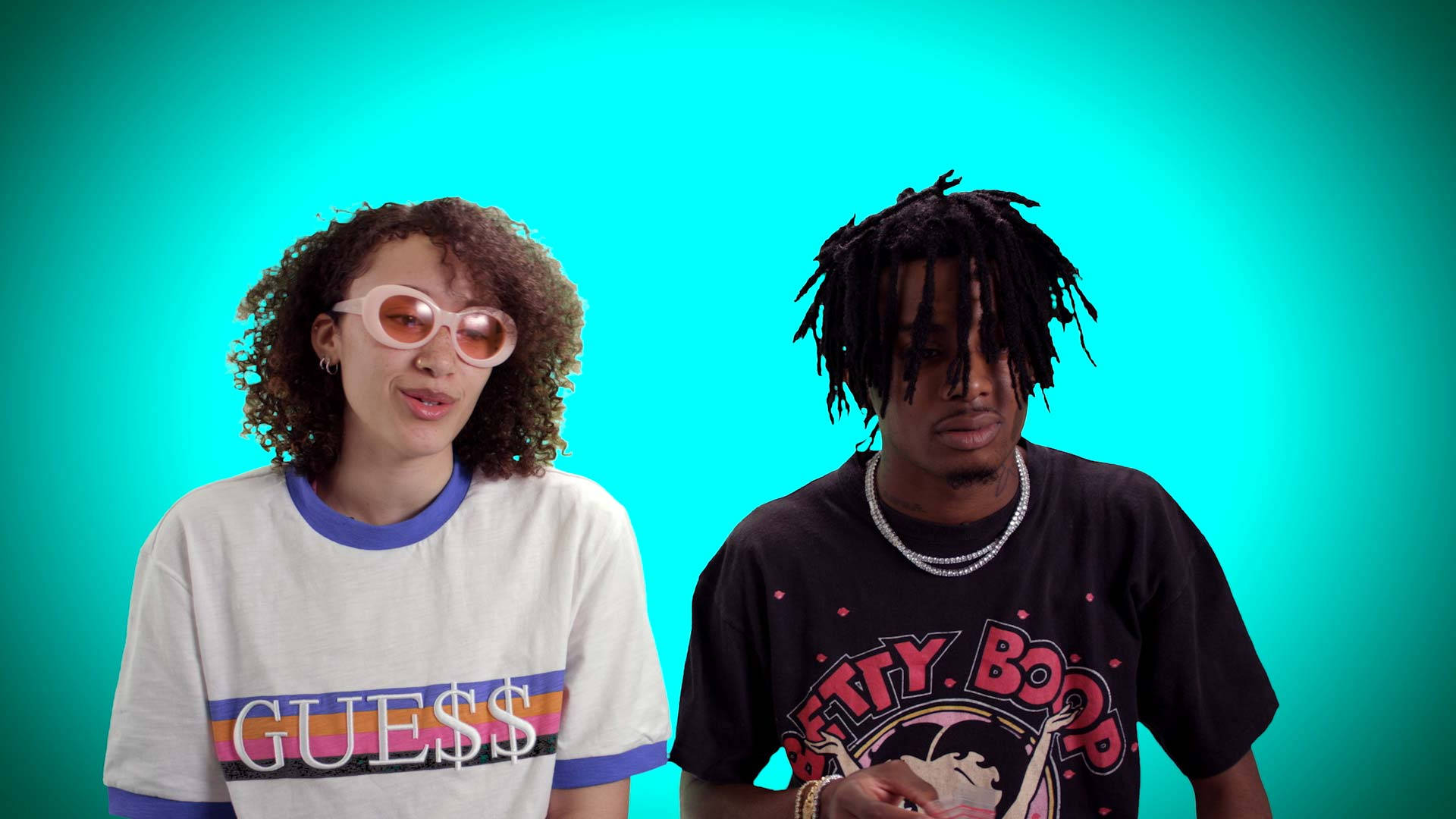 Carti 桌布 壁紙 — 兩位時尚打扮的人士在充滿活力的青綠色背景前擺姿勢，戴著大膽的太陽眼鏡和品牌T恤。