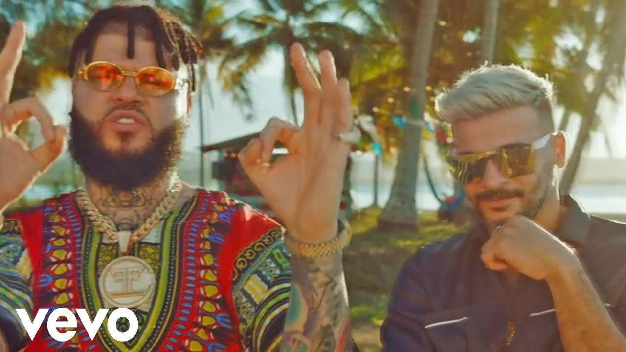 farruko 桌布 壁紙 — 兩位時尚男士戴著太陽眼鏡，在熱帶海灘背景襯托下自信地擺出OK手勢，背景有棕櫚樹。