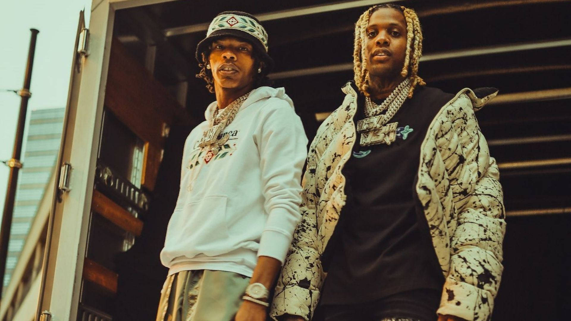 Lil Durk 桌布 壁紙 — 兩位時尚的饒舌歌手在粗獷的城市背景下，自信地穿著都市街頭服飾，配以大膽的珠寶和富有表現力的造型。