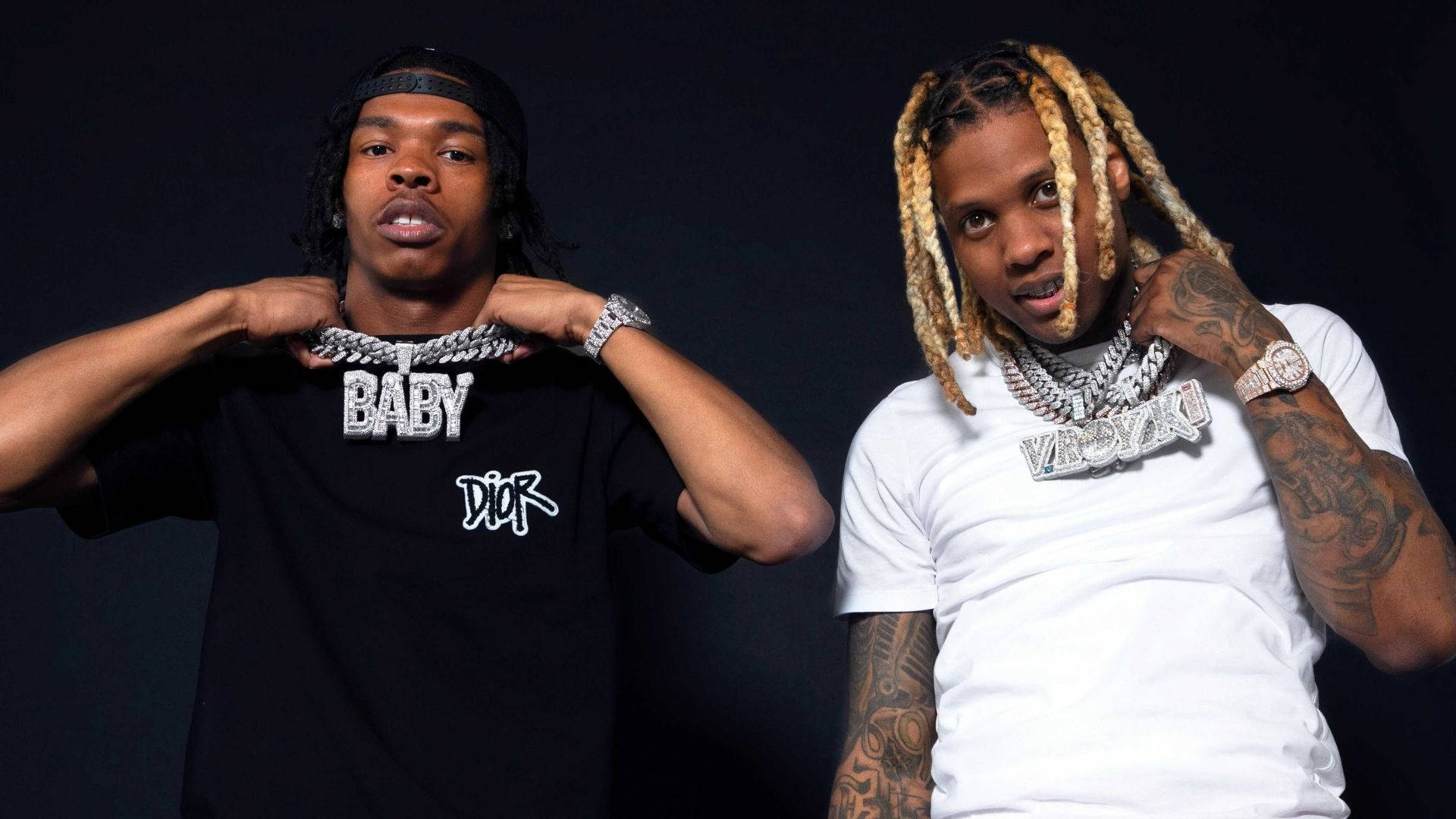 Lil Durk 桌布 壁紙 — 兩位時尚饒舌歌手在深色背景下自信擺姿勢，展示大膽珠寶和刺青。