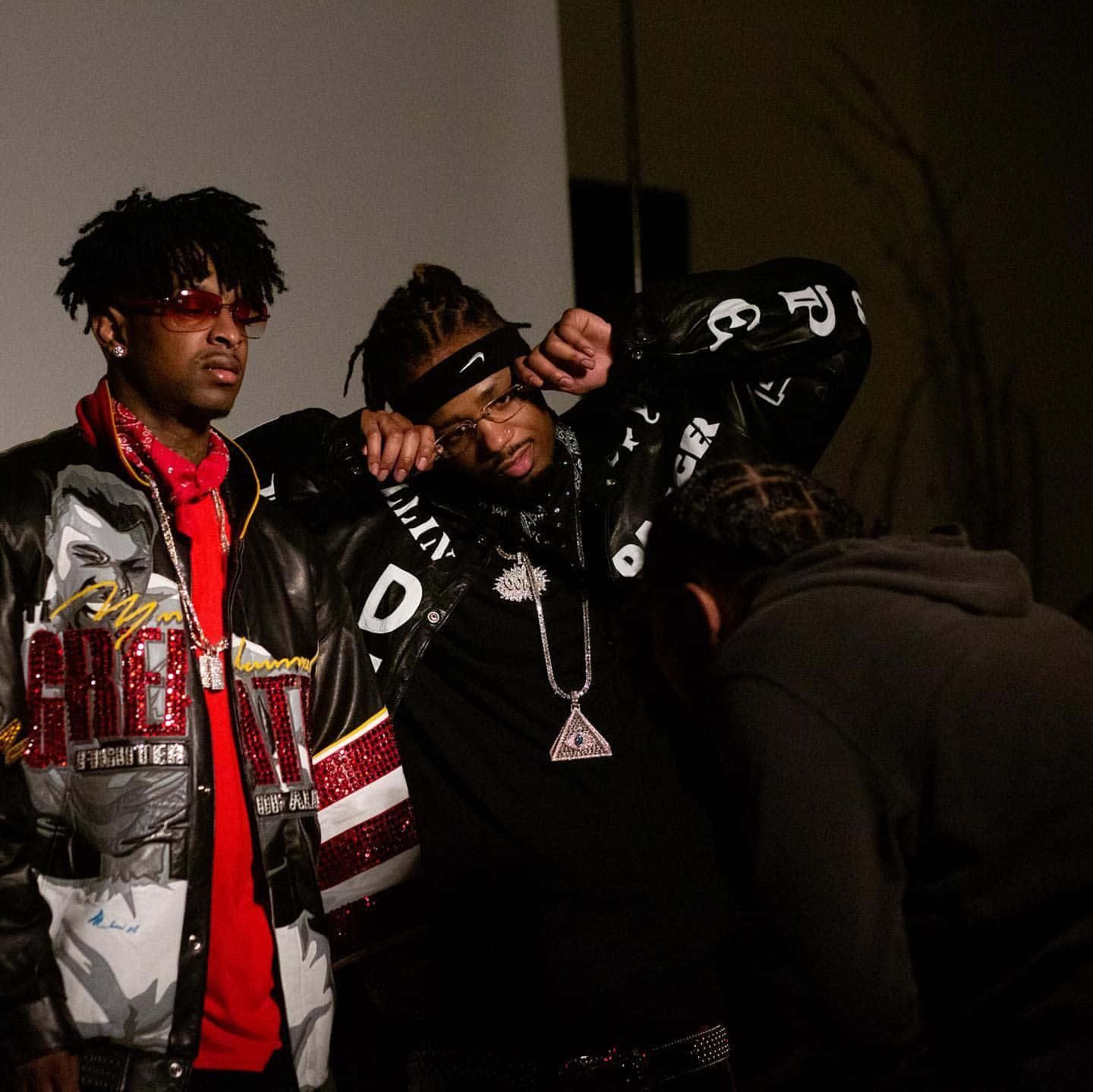 21 Savage 桌布 壁紙 — 兩位時尚饒舌歌手穿著大膽街頭服飾，在昏暗燈光下自信擺姿勢，第三人部分可見。
