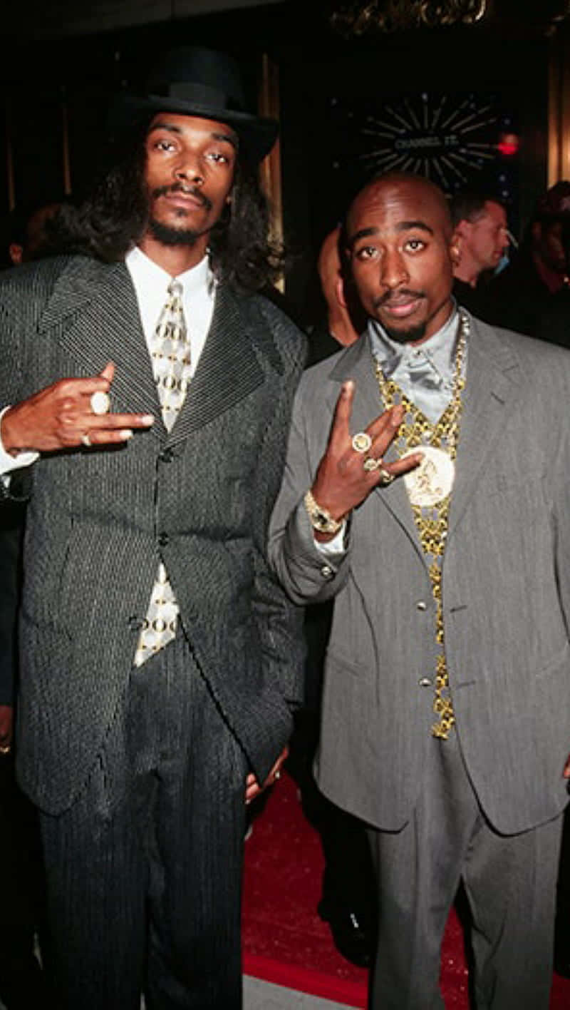 Young Snoop Dogg 桌布 壁紙 — 兩位標誌性嘻哈藝術家穿著俐落西裝和閃亮珠寶，在華麗的室內活動中自信擺姿勢。